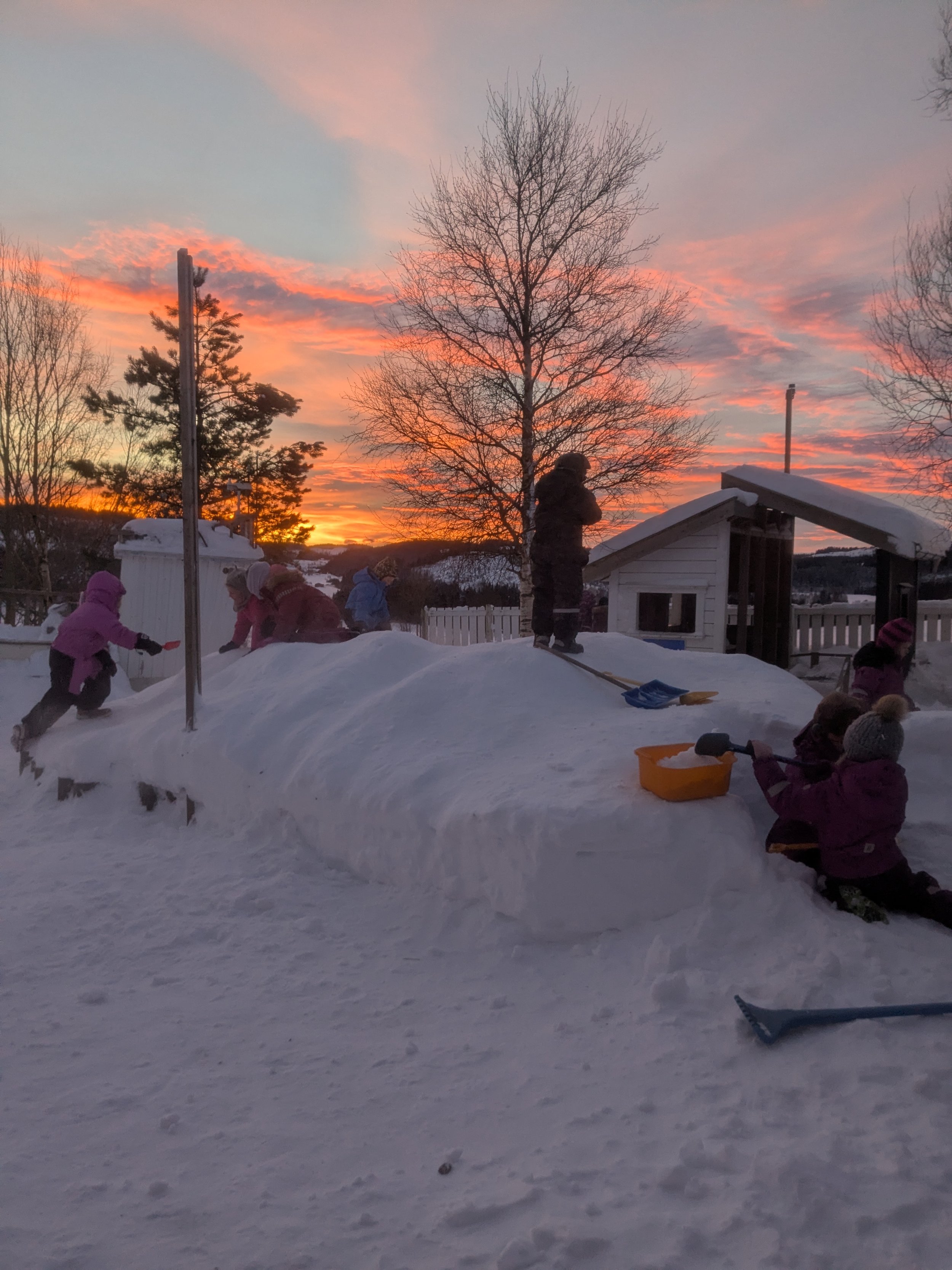 Barnehagen utendørs vinterstid, med rosa solnedgang