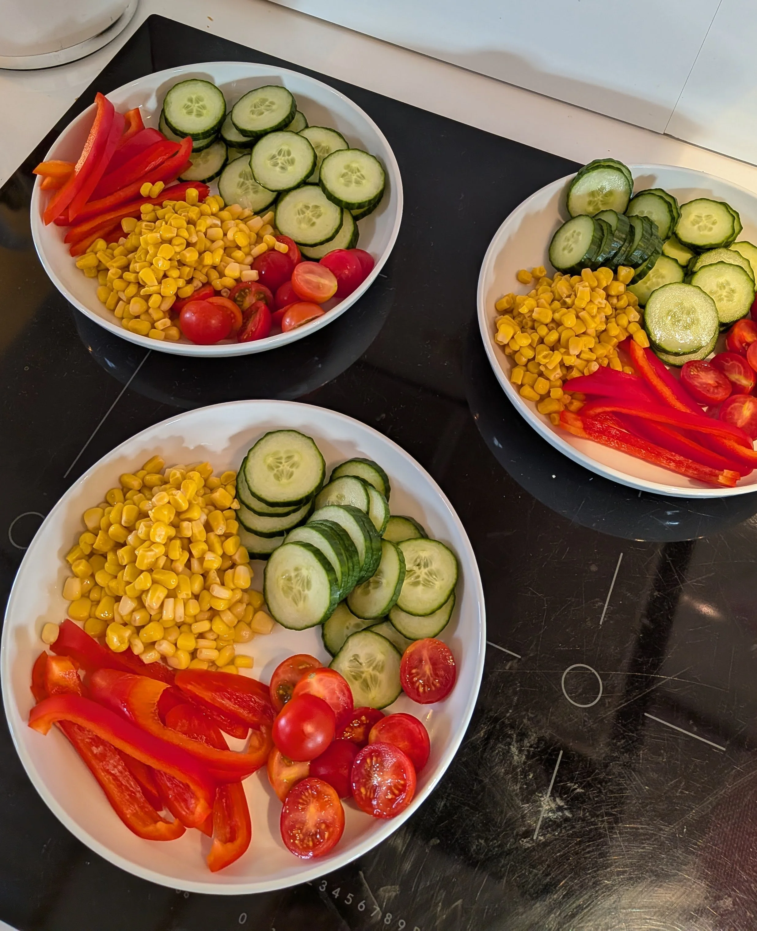 Tre hvit tallerkener med oppkuttede grønnsaker som agurk, tomater, paprika og mais.