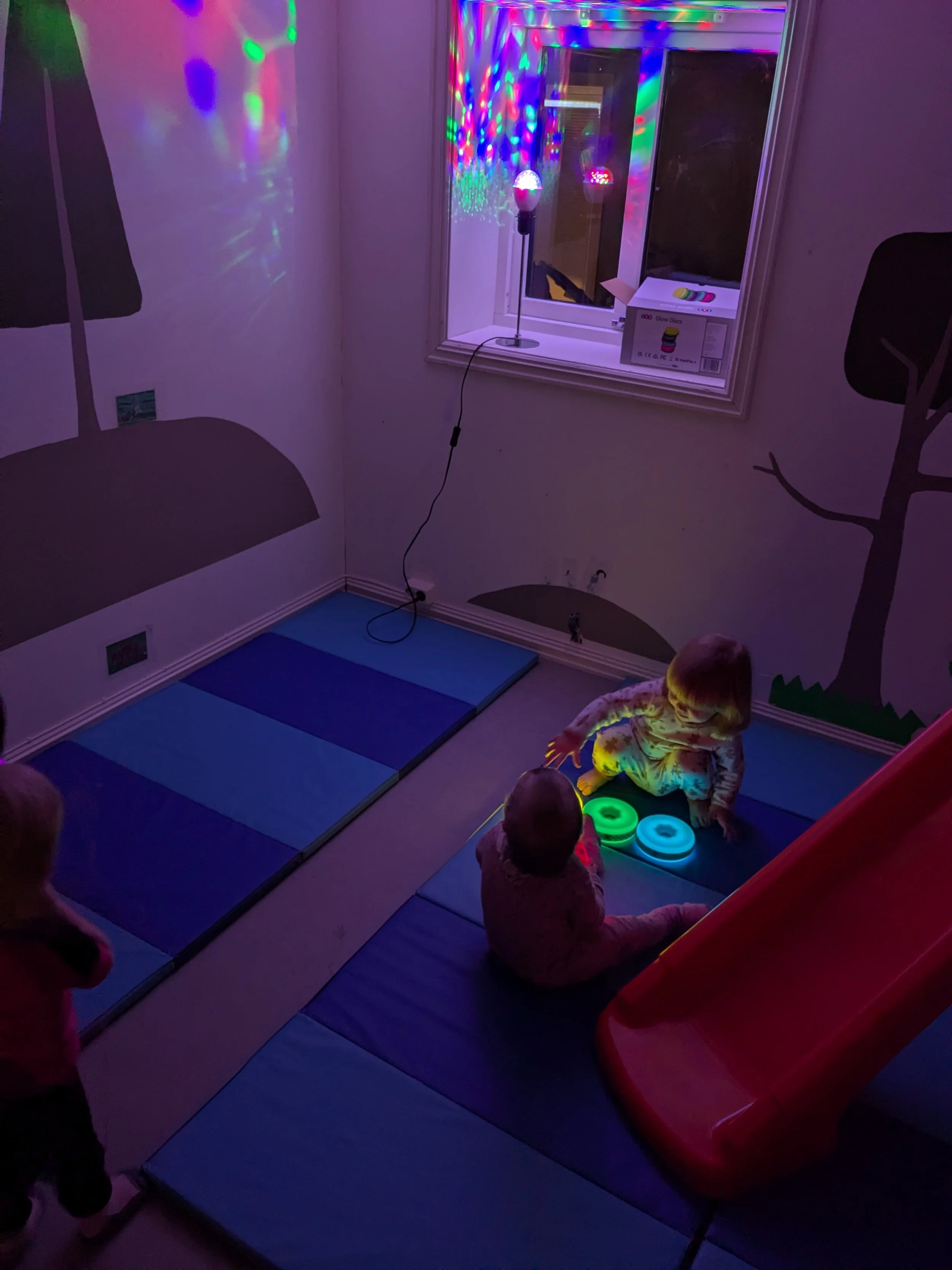 Et mørkt rom med fargerike lys. På gulvet er det yogamatter og puter