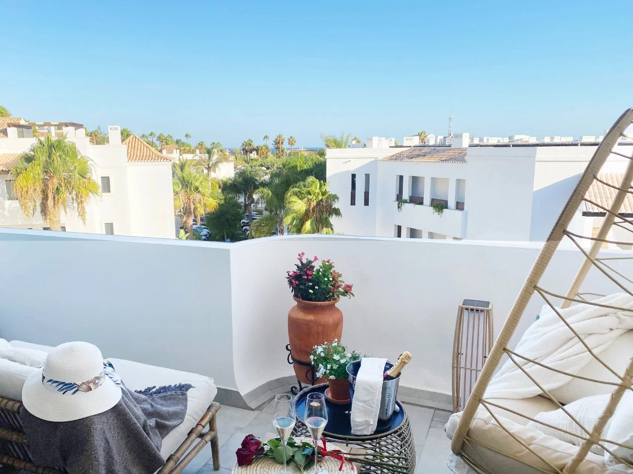 A scenic balcony view with chairs, a hat, and drinks, overlooking white buildings and palm trees under a clear blue sky. Holiday home in Lagos Algarve