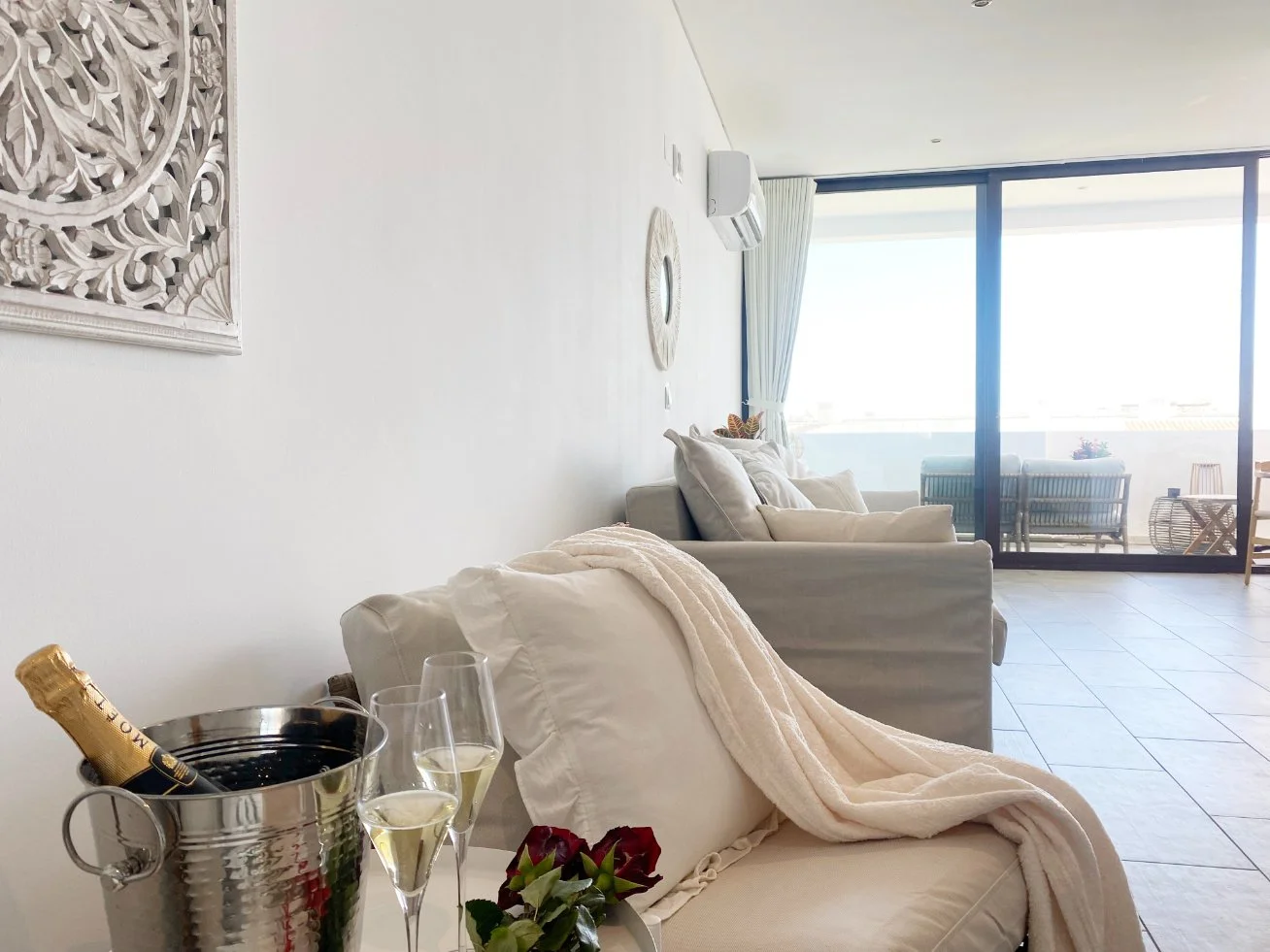 Living room with white sofas, champagne in an ice bucket, and champagne glasses, overlooking a balcony with outdoor seating. Holiday home in Lagos Algarve