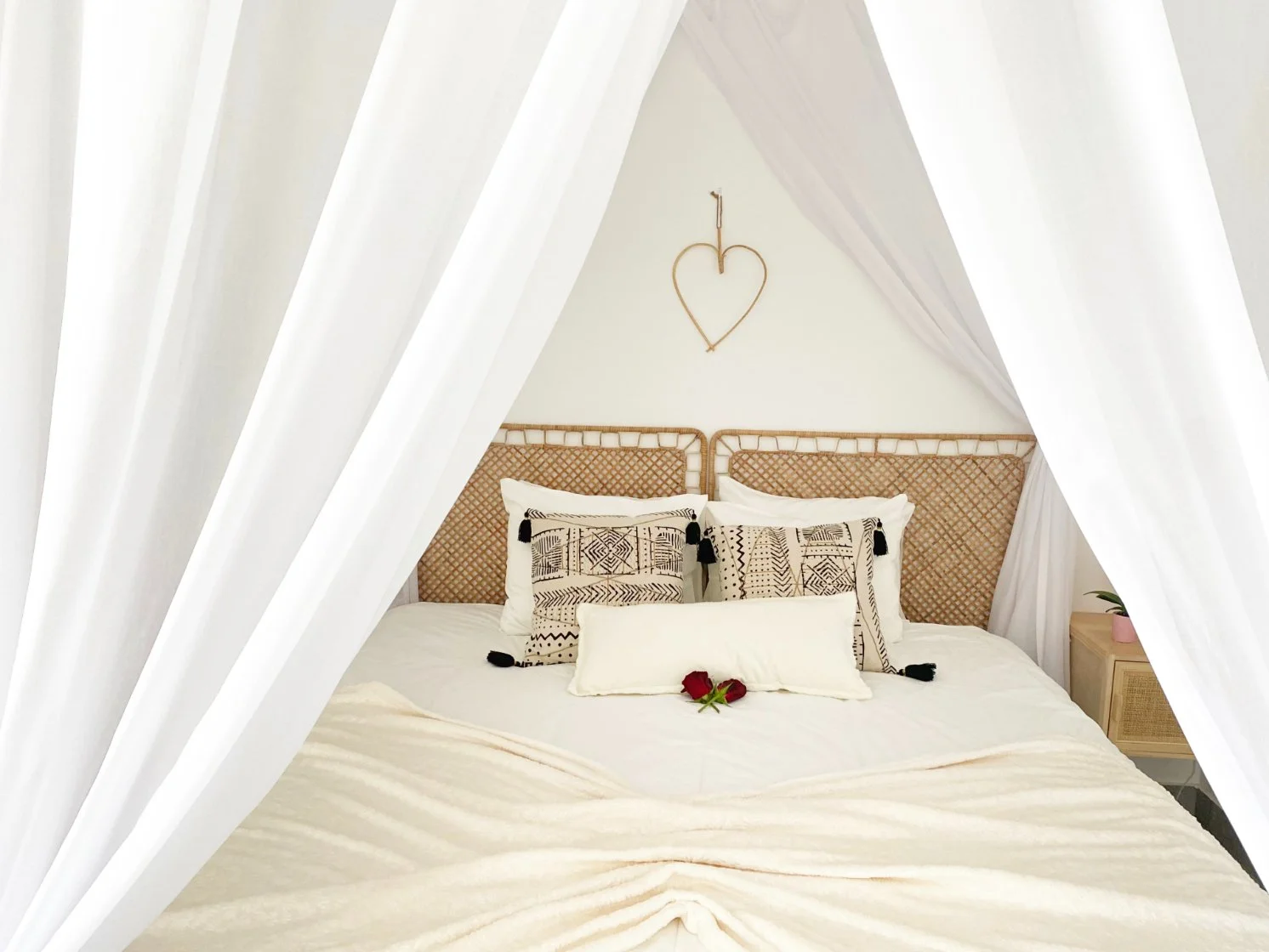 A neatly made bed with white linens and decorative pillows, surrounded by white curtains. There is a small wooden nightstand with a pink pot and a green plant. Holiday home in Lagos Algarve
