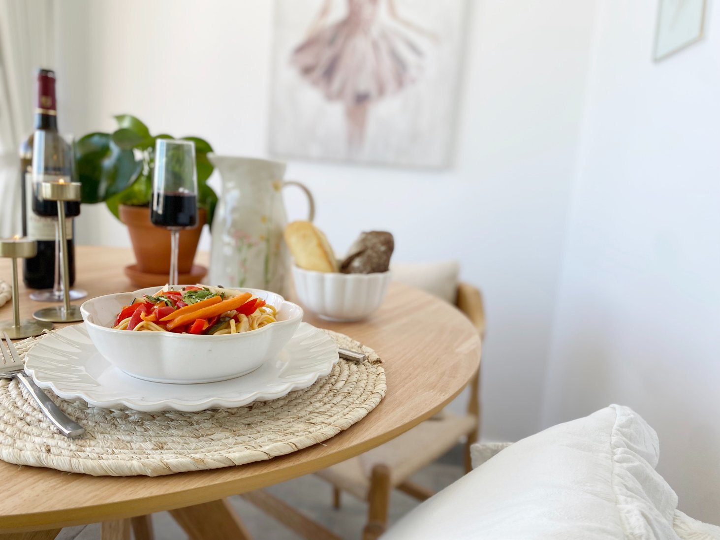 A bowl of pasta with vegetables on a wooden dining table with wine glasses, a potted plant, bread, and a pitcher in the background. Holiday home in Lagos Algarve