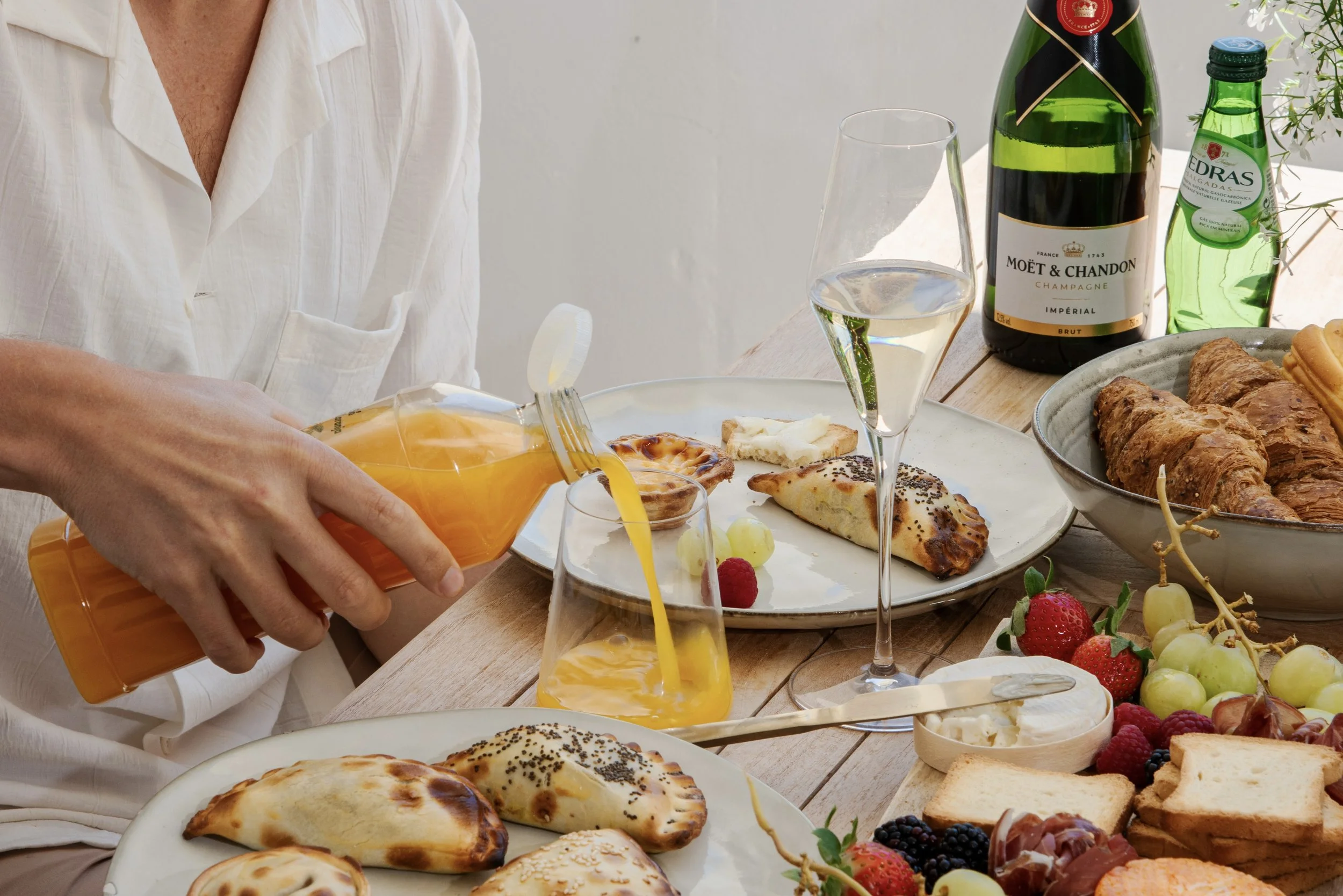 A breakfast table with pastries, fruit, a bottle of champagne, a glass of sparkling wine, orange juice being poured, and various food items. Holiday home in Lagos Algarve