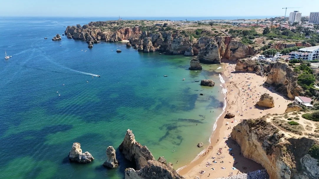 Aerial view of Lagos sandy beach surrounded by rocky cliffs with clear blue water and a few boats. Holiday home in Lagos Algarve