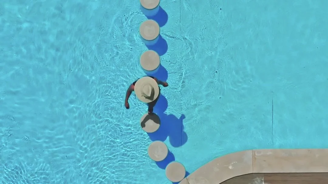Top-down view of a person wearing a large sunhat walking on round white stepping stones across a swimming pool. Holiday home in Lagos Algarve