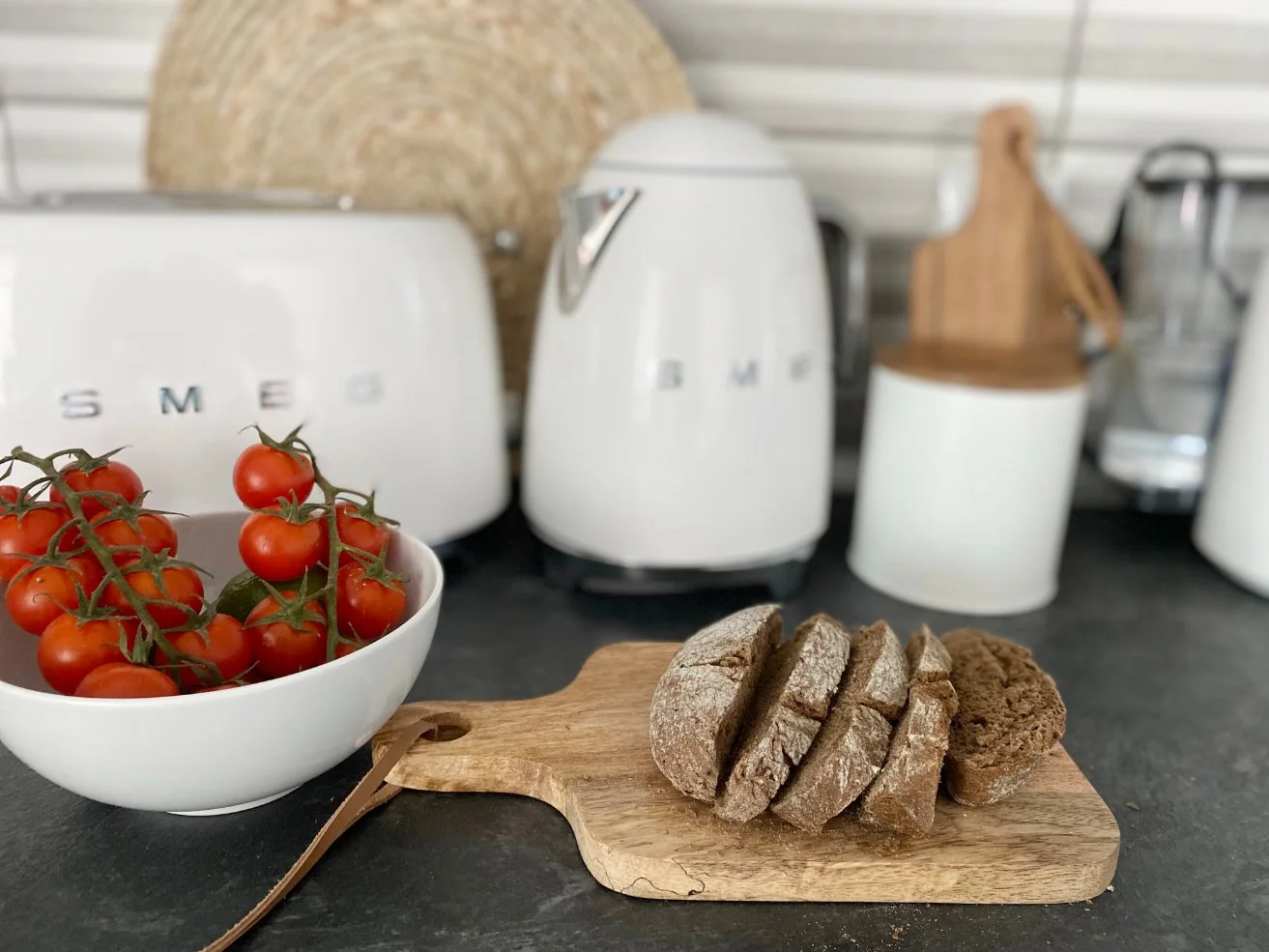 A bowl of cherry tomatoes on a vine, sliced bread on a wooden cutting board, and kitchen appliances in the background. Holiday home in Lagos Algarve