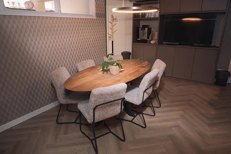 Eettafel met zes stoelen en een plant in een pot, in een modern ingerichte kamer met een keukenkast en tv.