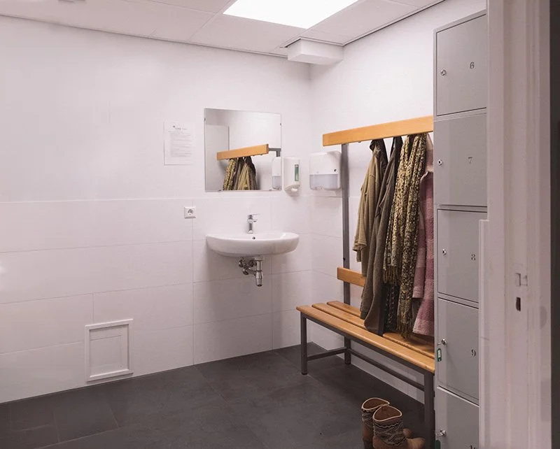 Kleedruimte met spiegel, veters en jassen hangend aan een houten rek, locksmithsprank, schoenen op de grond