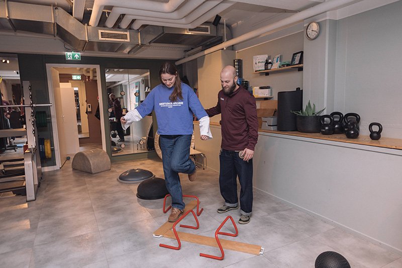 Goed Fysio Een vrouw oefent op een cerebrale training bank onder begeleiding van een instructeur in een sportschool.