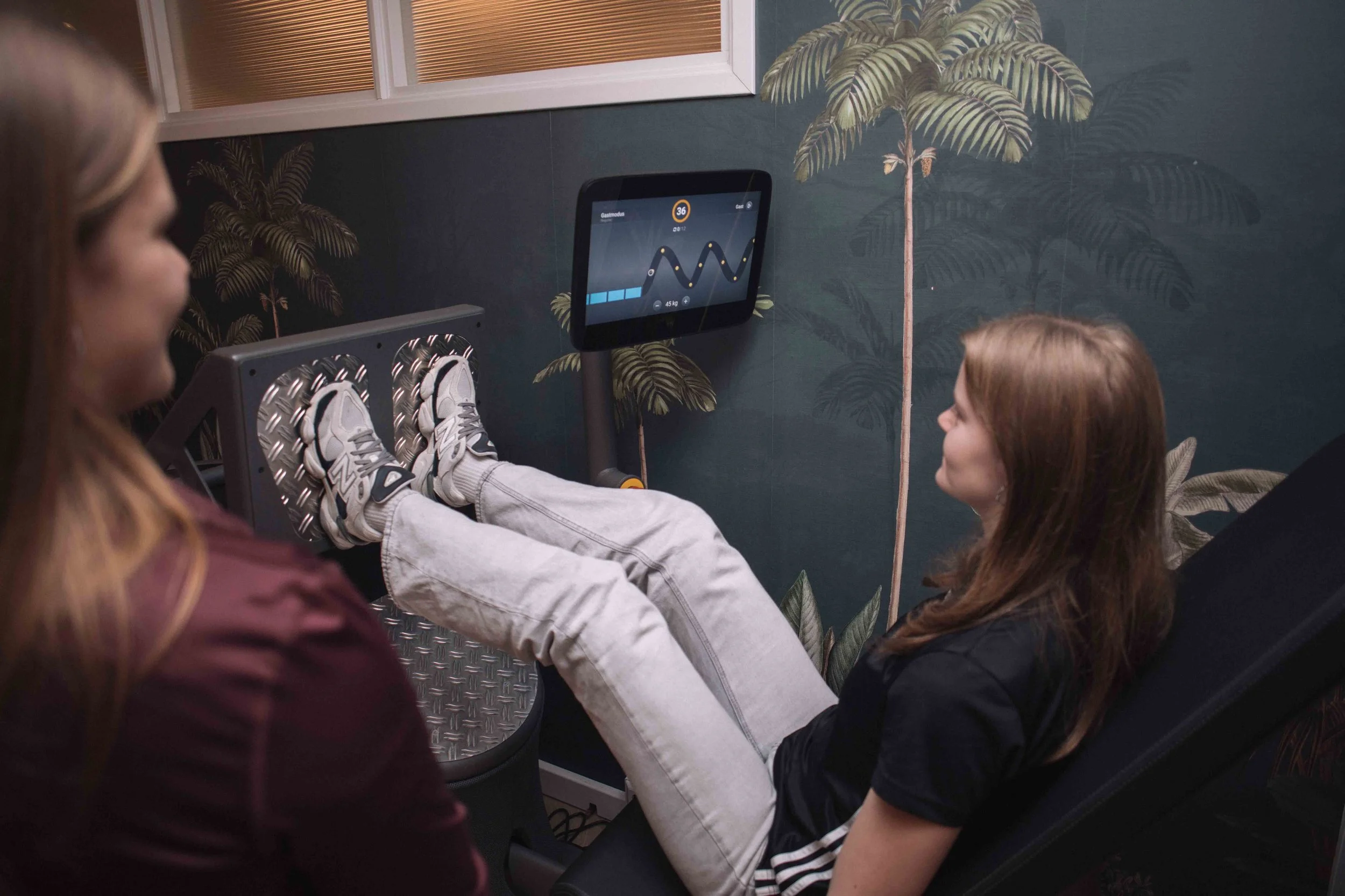 Goed Fysio Een persoon op een loopband die een fitnessmonitor bedient in een kamer met serpentijnachtige wanddecoraties en planten.