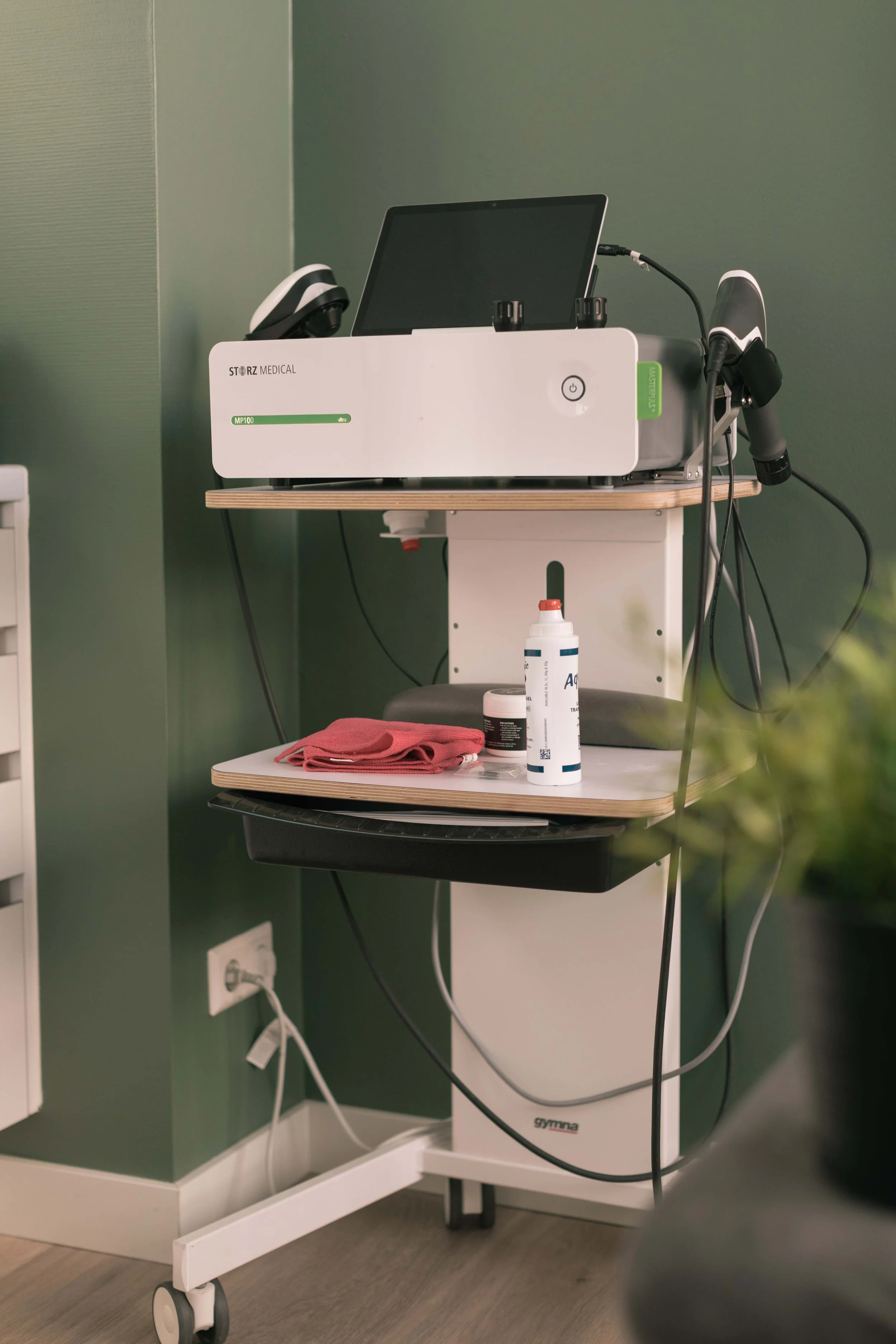 Goed Fysio Een medische machine op een houten tafel met diverse medische spullen en een groene muur op de achtergrond.