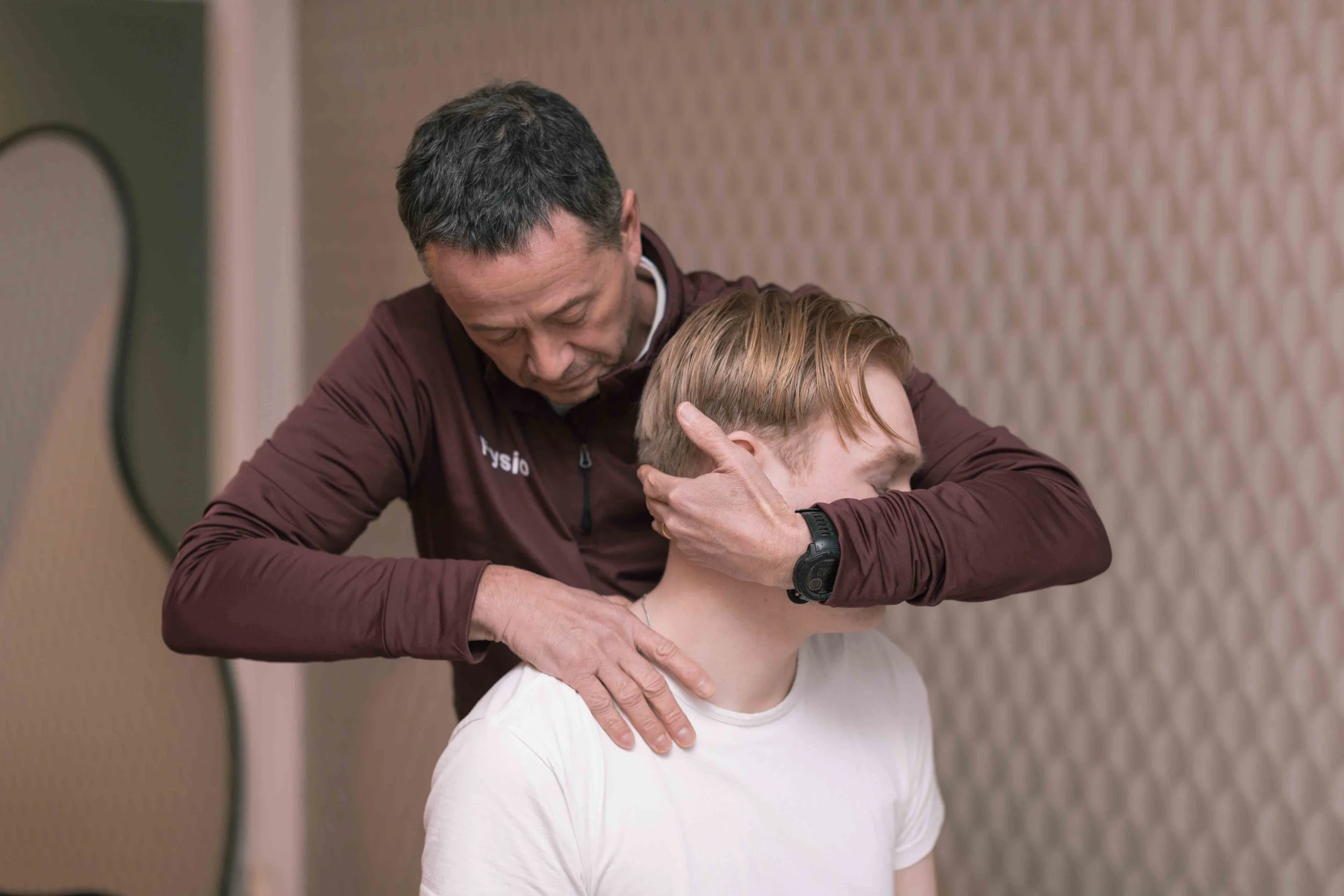 Goed Fysio Een man die fysiotherapie doet met een jonge patiënt, in een kamer met een ronde spiegel en een beige muur.