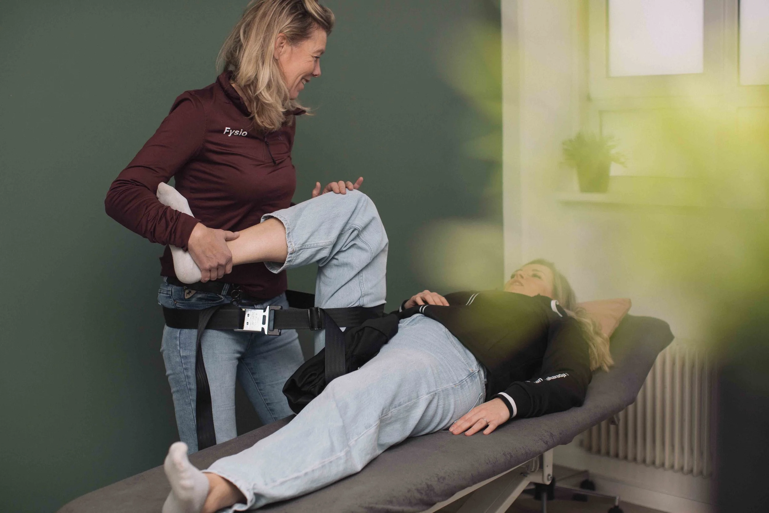 Goed Fysio Een fysiotherapeut houdt een kniebandage vast terwijl een patiënt op een behandeltafel ligt, in een fysiotherapiepraktijk.