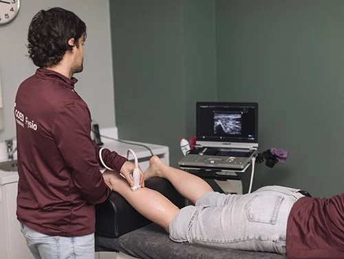 Medisch onderzoek waarbij een arts een echografie op het bovenbeen van een patiënt uitvoert, met een monitor die de beelden weergeeft.