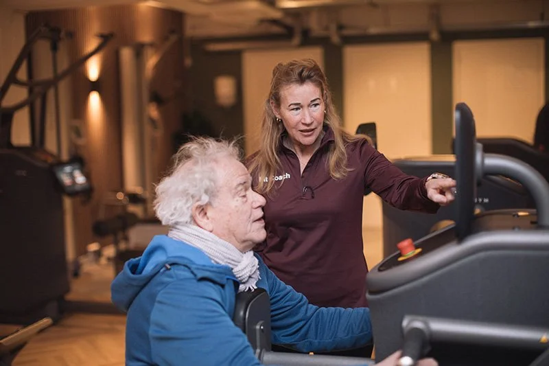 Goed Fysio Een vrouw die een oudere man begeleidt terwijl hij op een loopband traint in een fitnessruimte.
