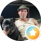 Man met hoed en een grote zwart-witte hond op zijn schoot, zittend voor een zwarte achtergrond.