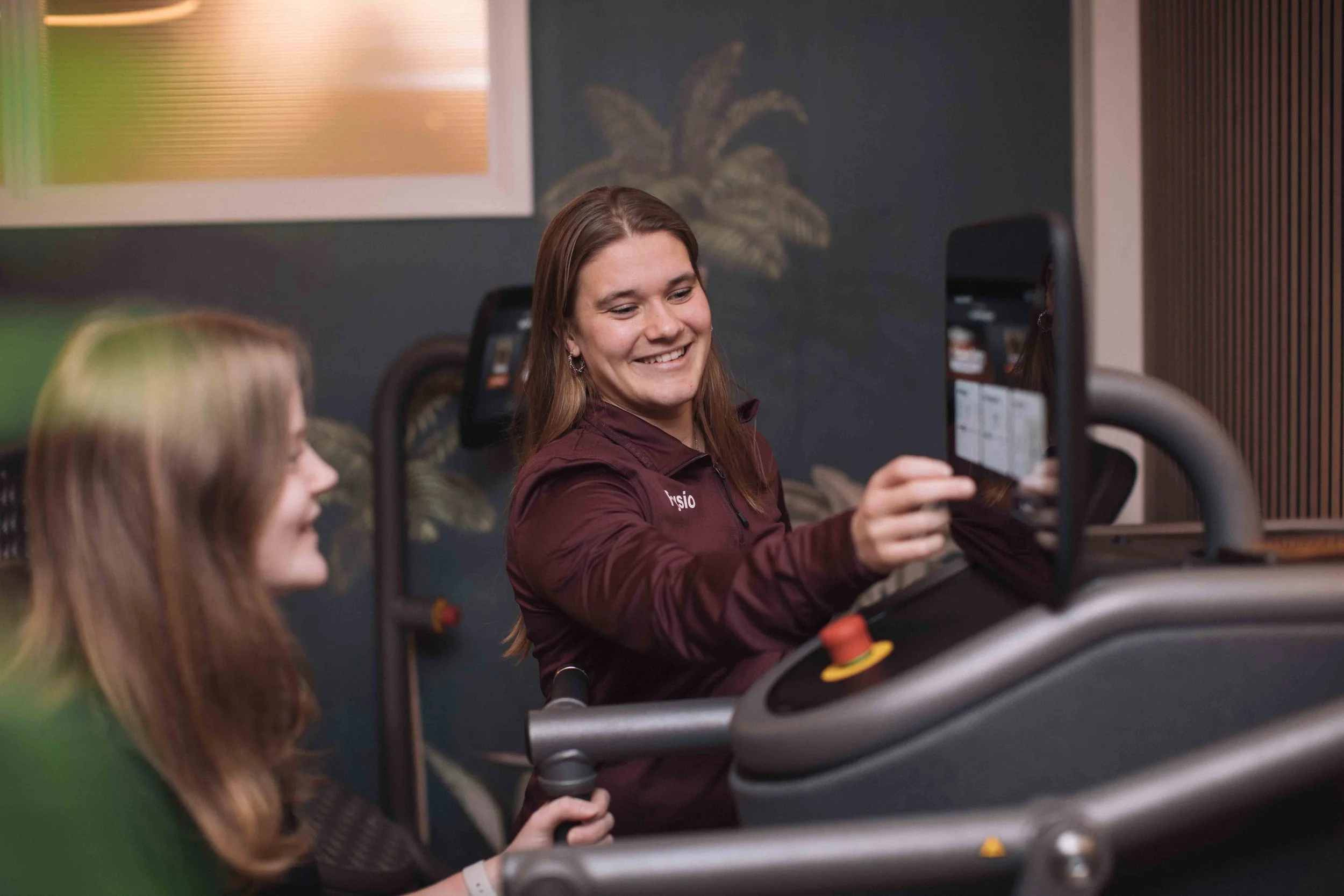 Vrouw en meisje die zich in een indoor sportomgeving bevinden, lachend en samen aan een fitnessapparaat werken.
