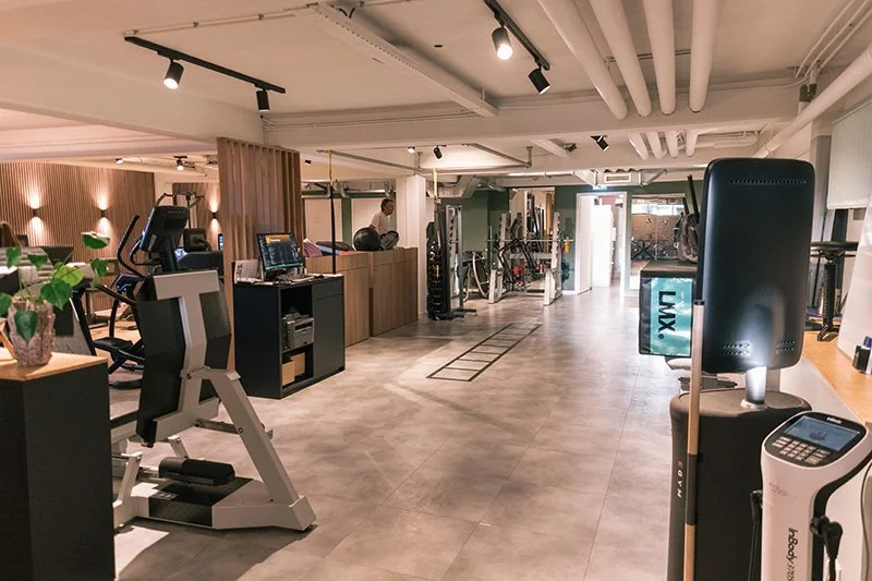 Fitnessruimte met cardio- en krachtapparatuur, waaronder loopbanden, fietsen en gewichten, in een modern, goed verlichte sportschool.