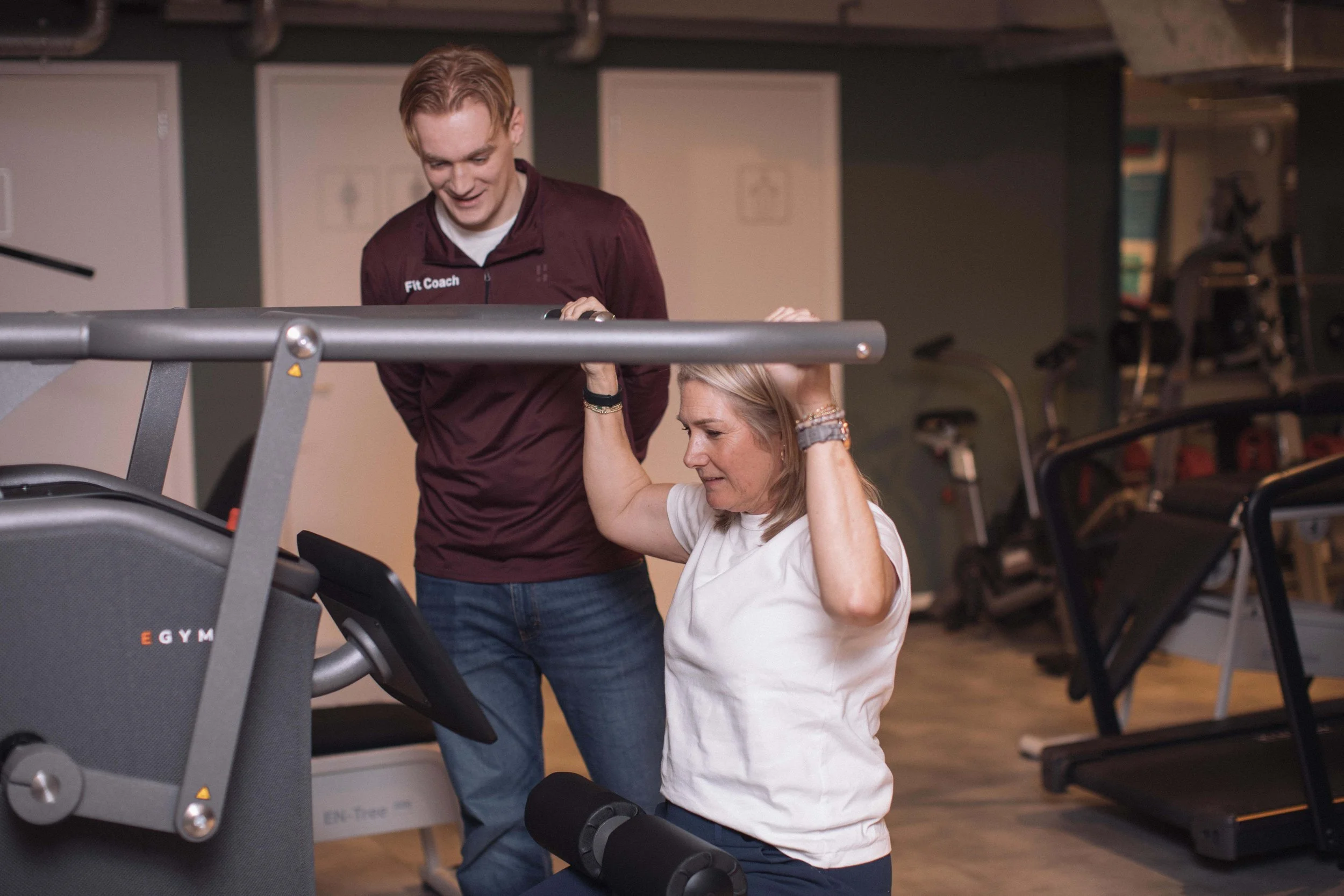 Goed Fysio Een man met een sportoutfit en een vrouw aan een loopband in een sportschool. De man helpt de vrouw met haar workout.