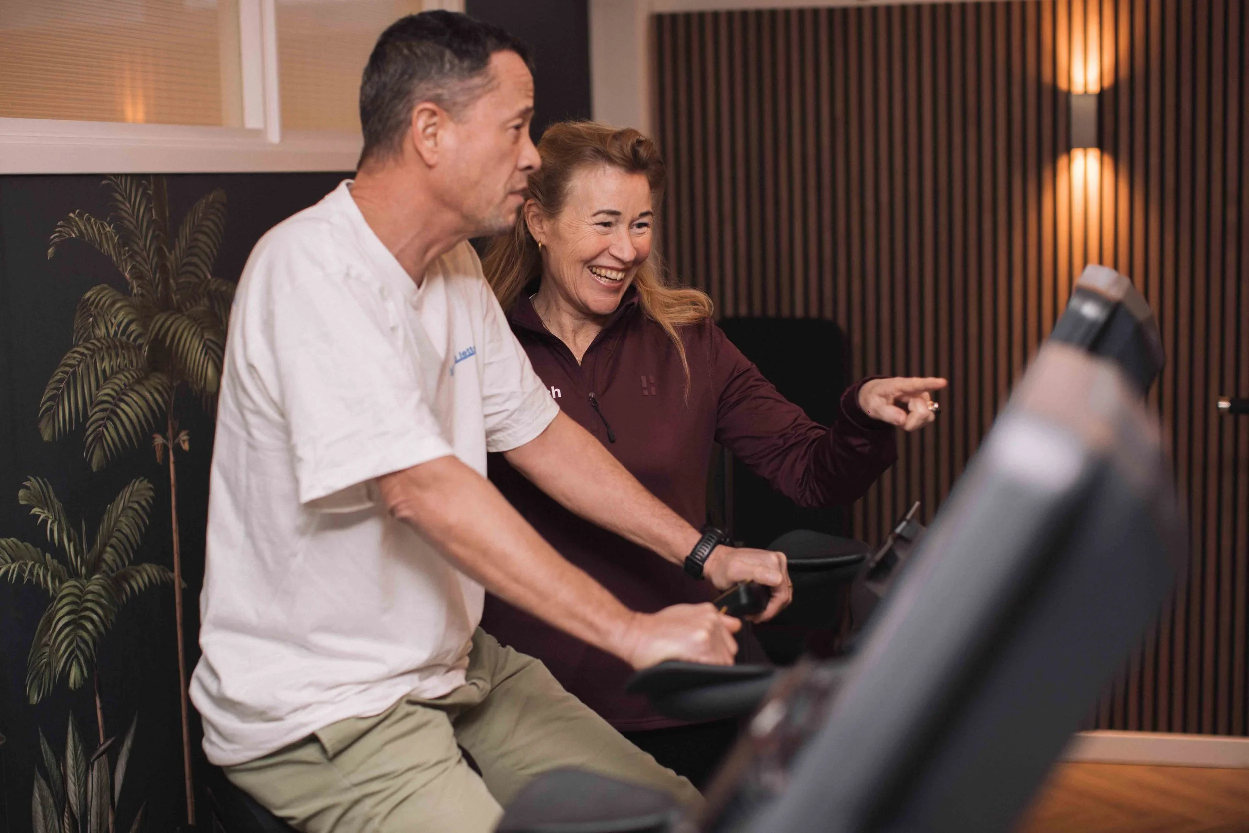 Twee mensen, een man en een vrouw, lachen terwijl ze samen naar een computerscherm kijken in een rustige, modern ingerichte kamer.