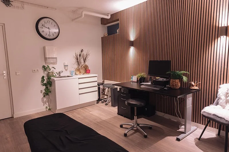 Een recreatieruimte met een zwart bankje, witte kast, planten, een computerbureau, een bureau en een stoel, met houten wandbekleding en muurverlichting.