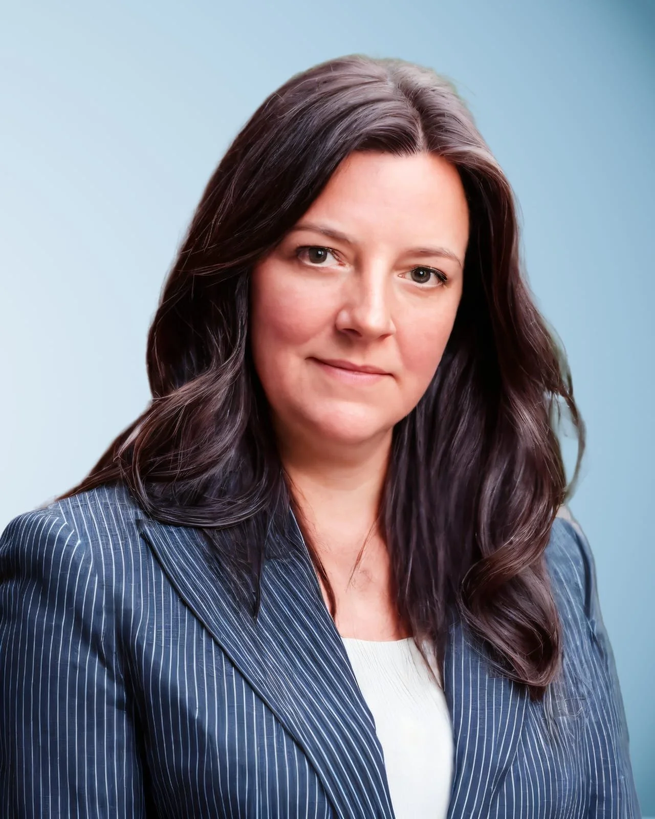 Portrait d'une femme avec des cheveux bruns foncés, portant une veste à rayures bleues et un haut blanc, contre un fond bleu clair.