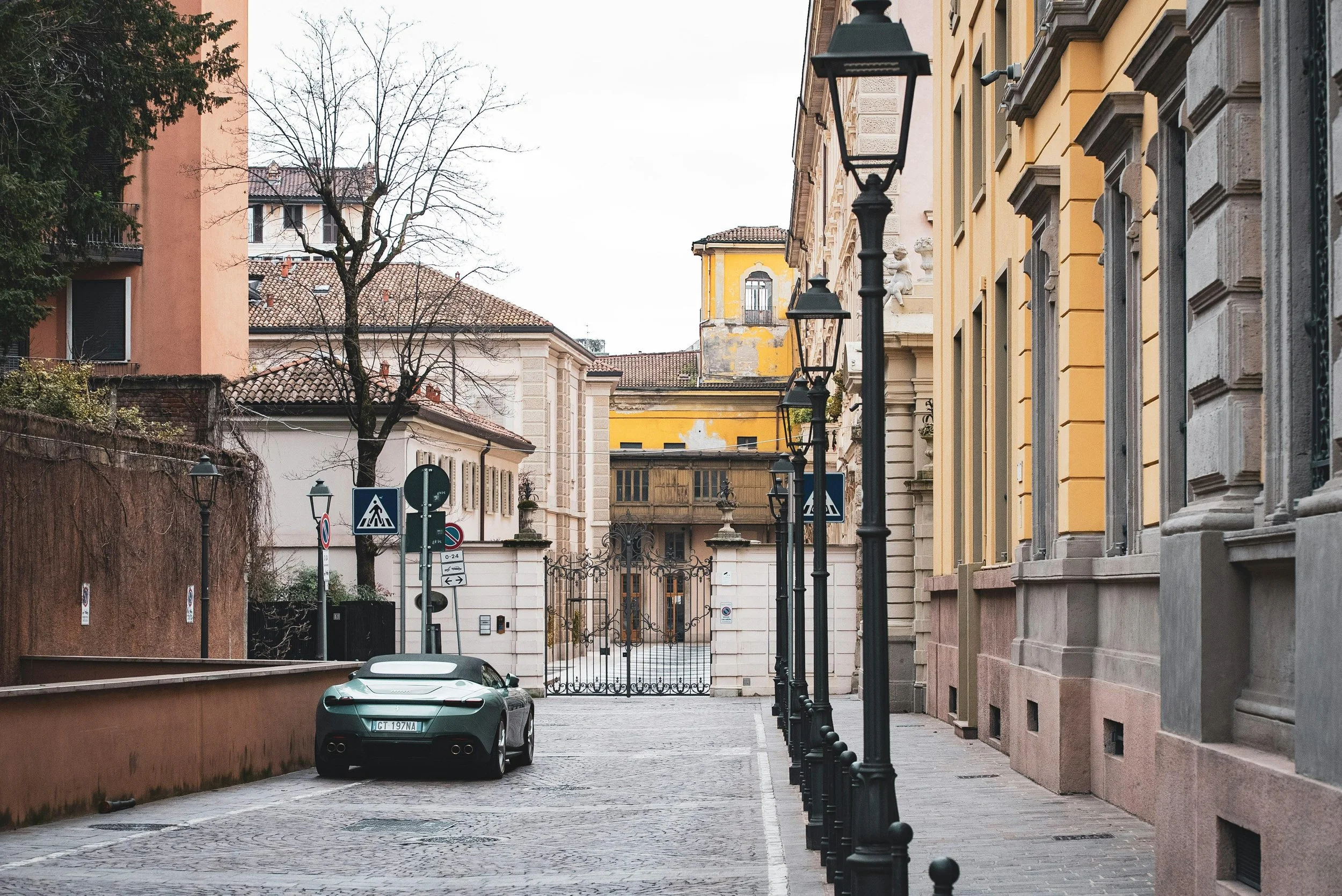 Strada di città con lampioni, macchina sportiva nera parcheggiata, edifici storici e segnaletica stradale