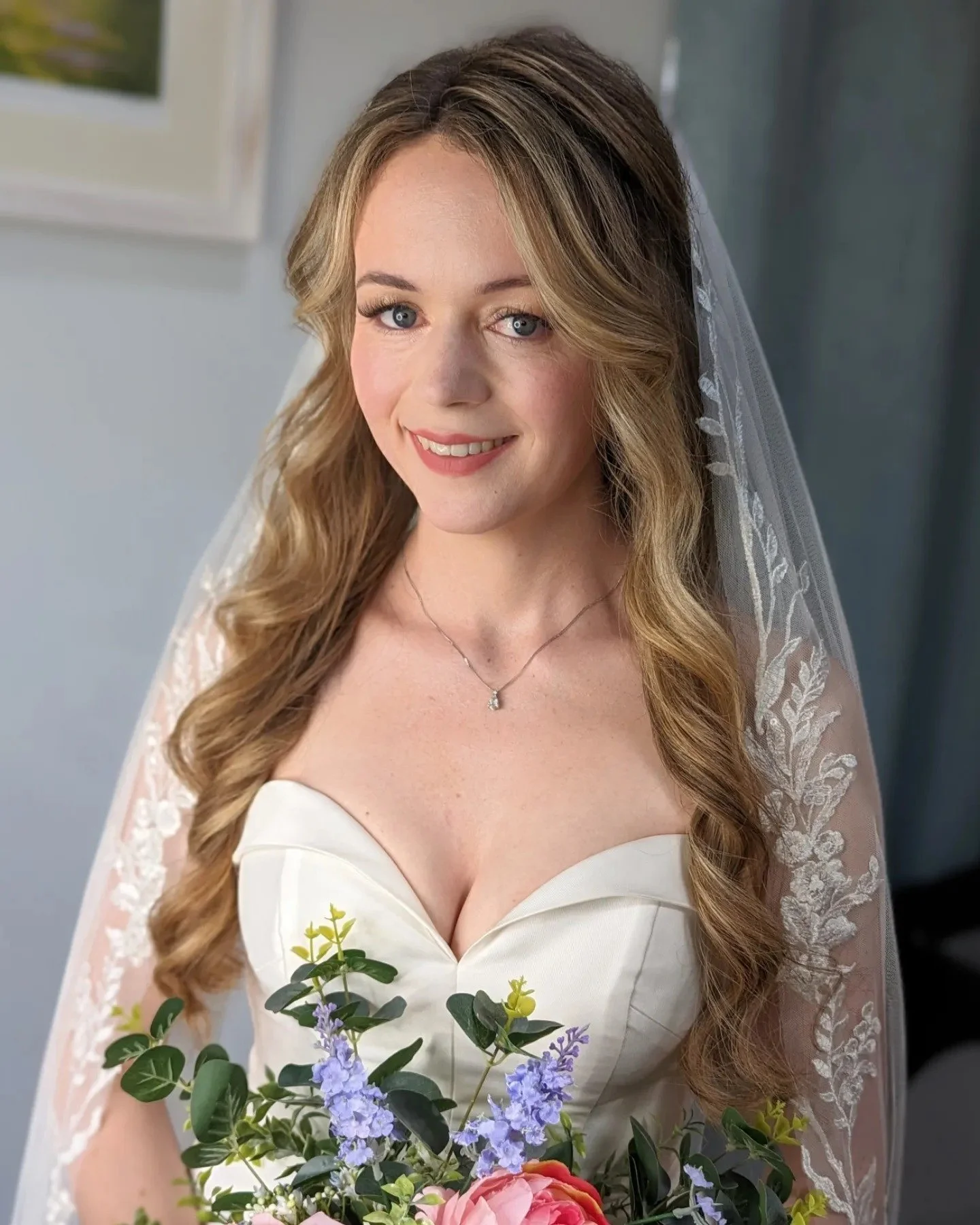 A bride smiling and holding a bouquet of flowers, wearing a white wedding dress and veil.