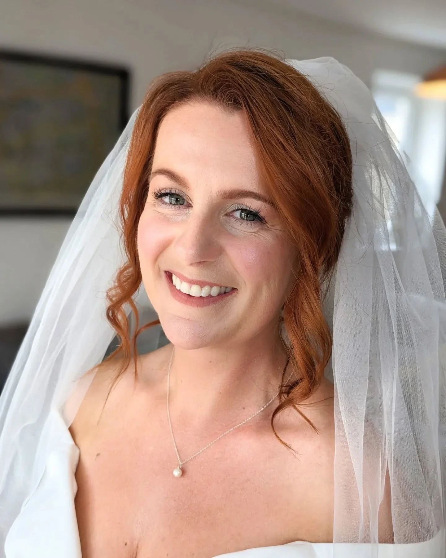 A smiling woman with red hair in a wedding dress and veil.