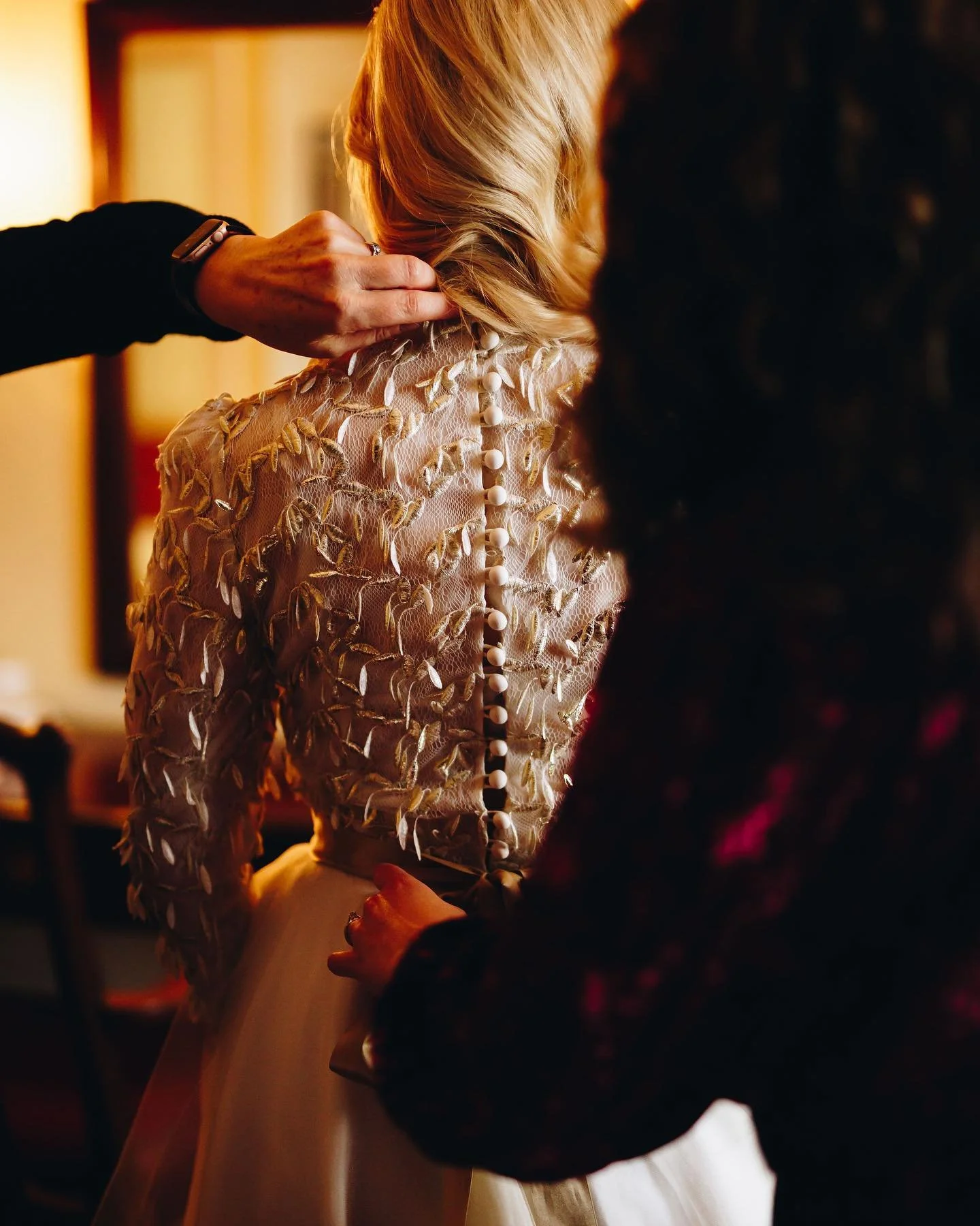 A woman in an elegant dress is being assisted with her outfit, likely getting dressed or prepared for a special event.
