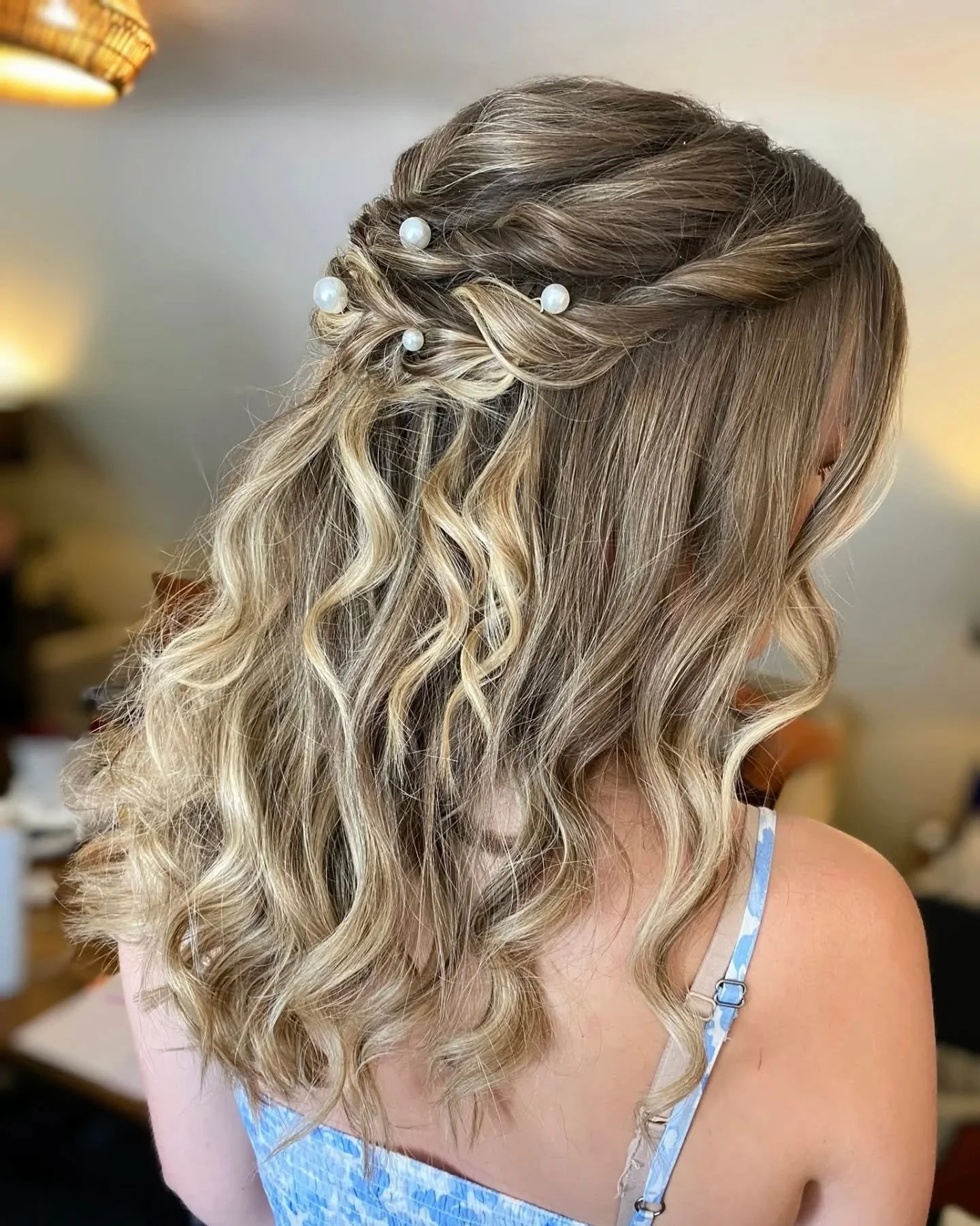 Woman with shoulder-length wavy blonde hair styled with small pearl hairpins