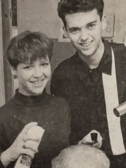 Two teenagers, a boy and a girl, smiling and standing close together in black and white photograph.