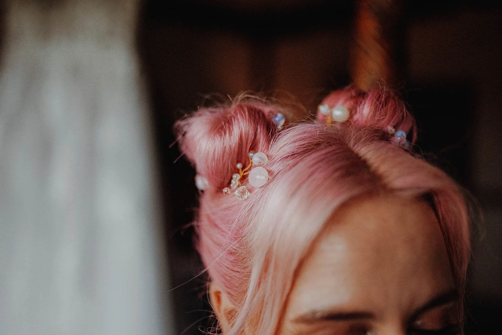 Close-up of a woman's pink hair styled into buns decorated with beads and pearls