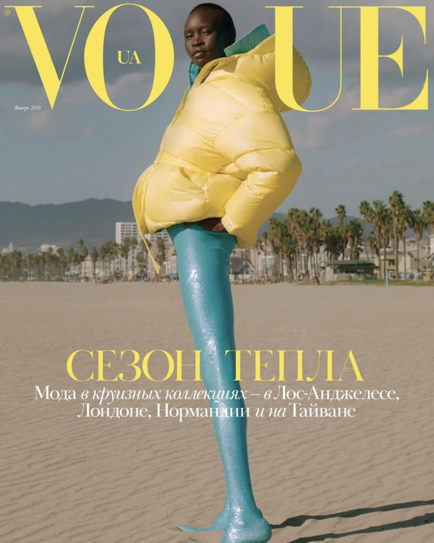 Magazine cover with a person standing on a beach, wearing a yellow puffy jacket and teal pants, with palm trees in the background. The cover has large yellow text reading 'VOGUE UA' and additional text in Cyrillic script.
