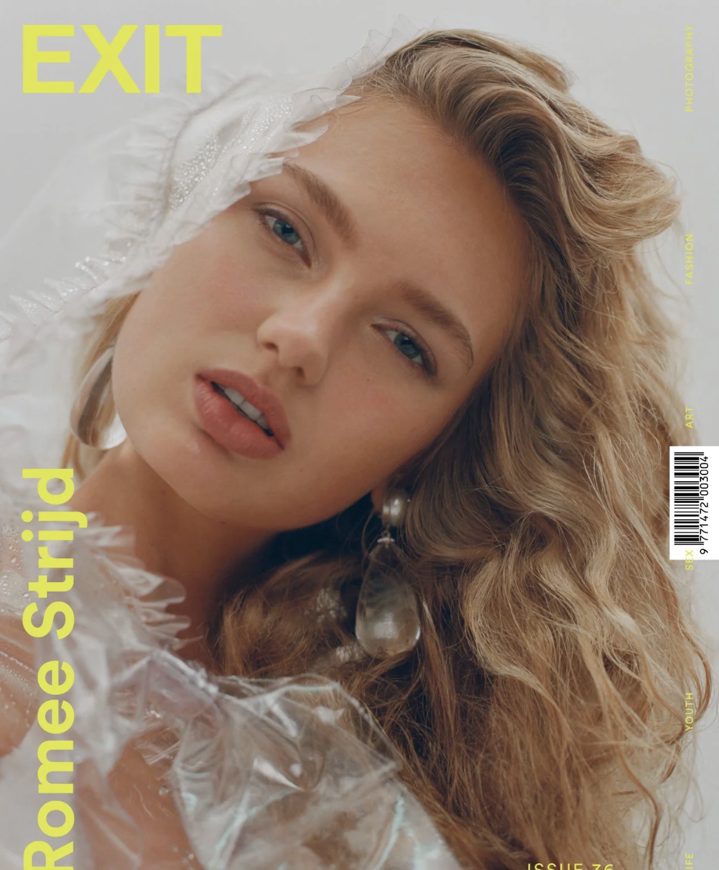 Close-up of a woman with red hair and blue eyes, surrounded by clear plastic and wearing pearl earrings, with yellow text on a magazine cover.