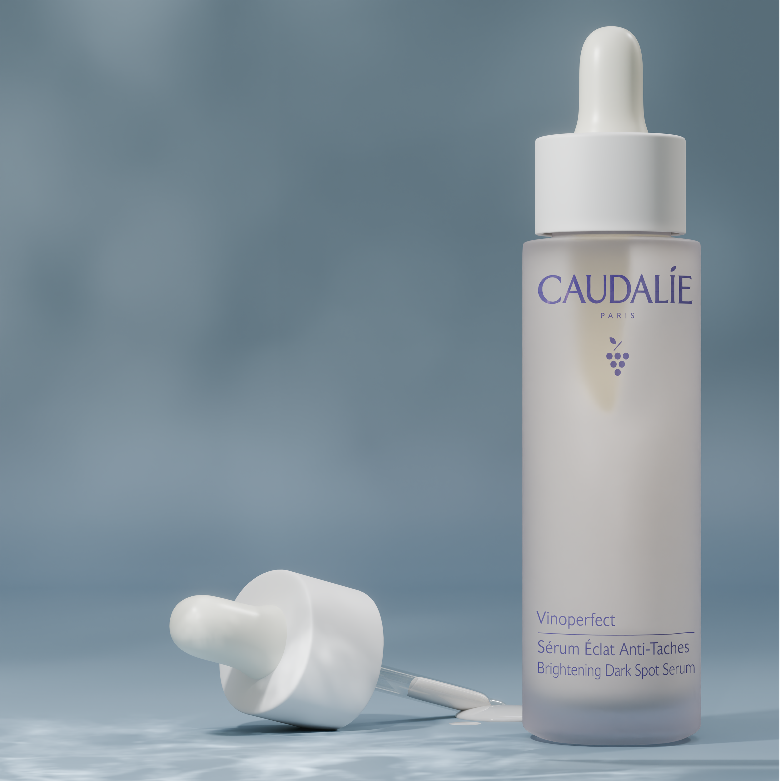 A white bottle of Caudalíe Brightening Dark Spot Serum on a reflective surface with a blurred background.