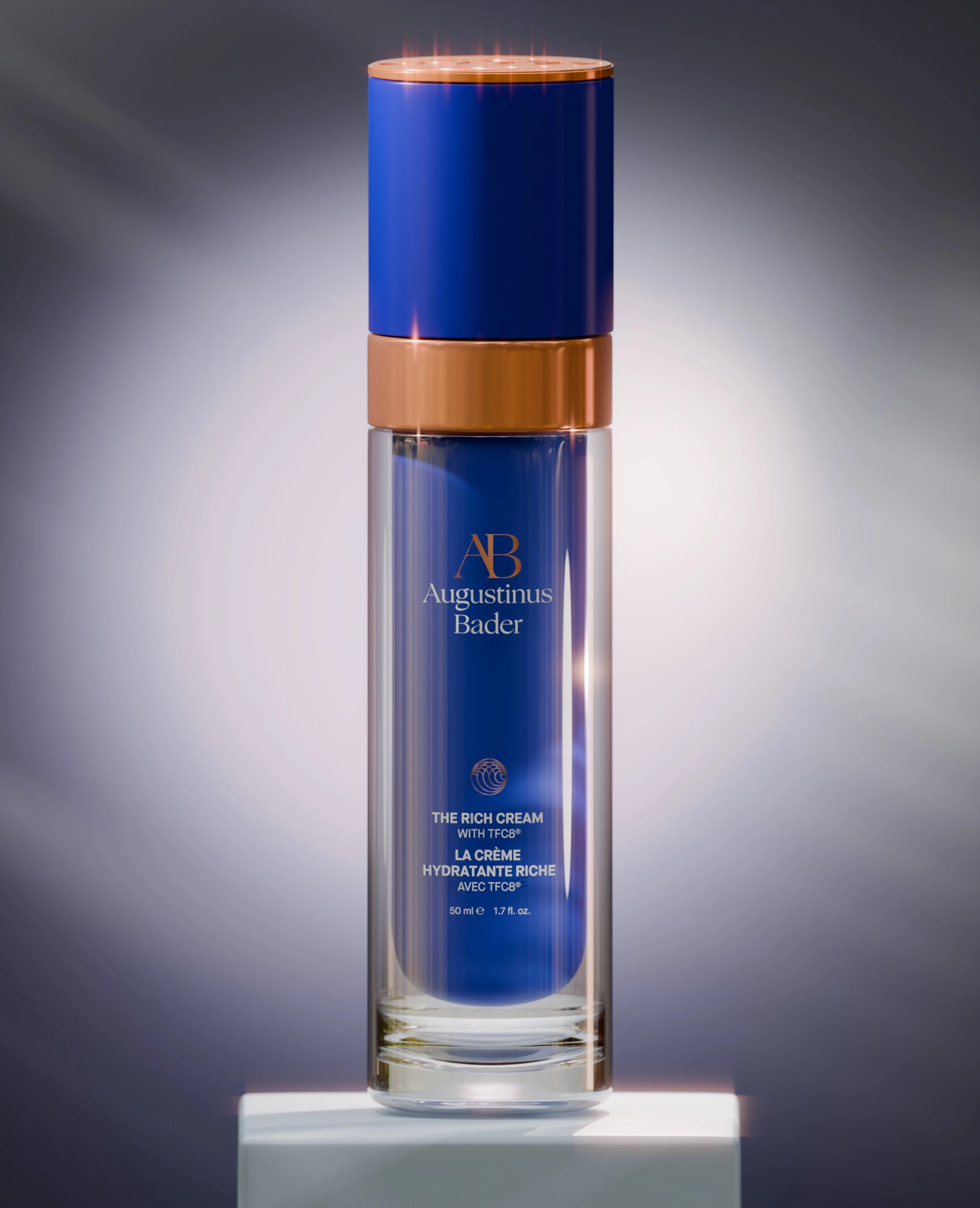 A tall cylindrical skincare product bottle with a blue body, metallic rose gold cap, and base, placed on a white pedestal, with a gradient gray background.