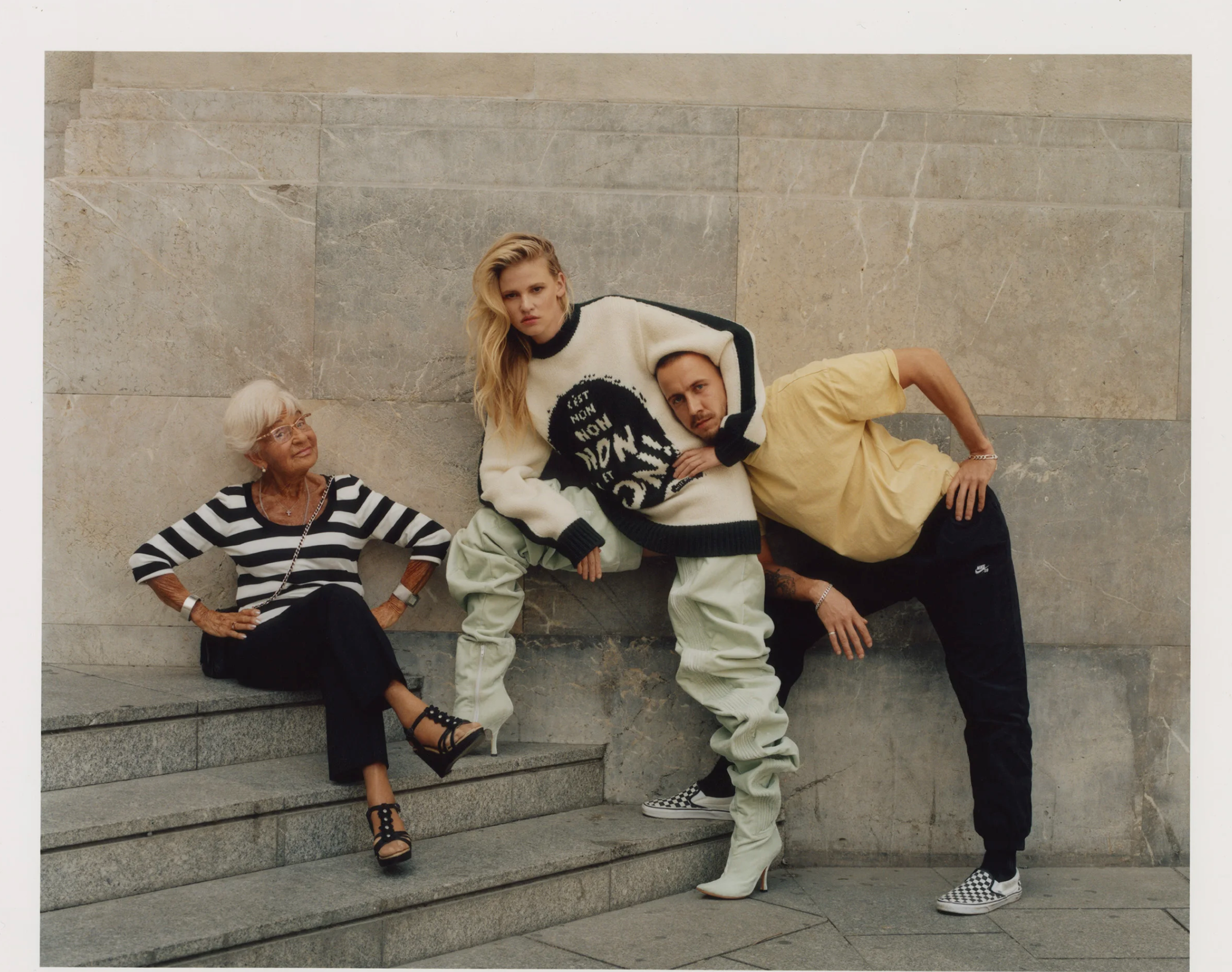 Four people sitting and lying on stone steps against a stone wall, with casual clothing and various expressions.