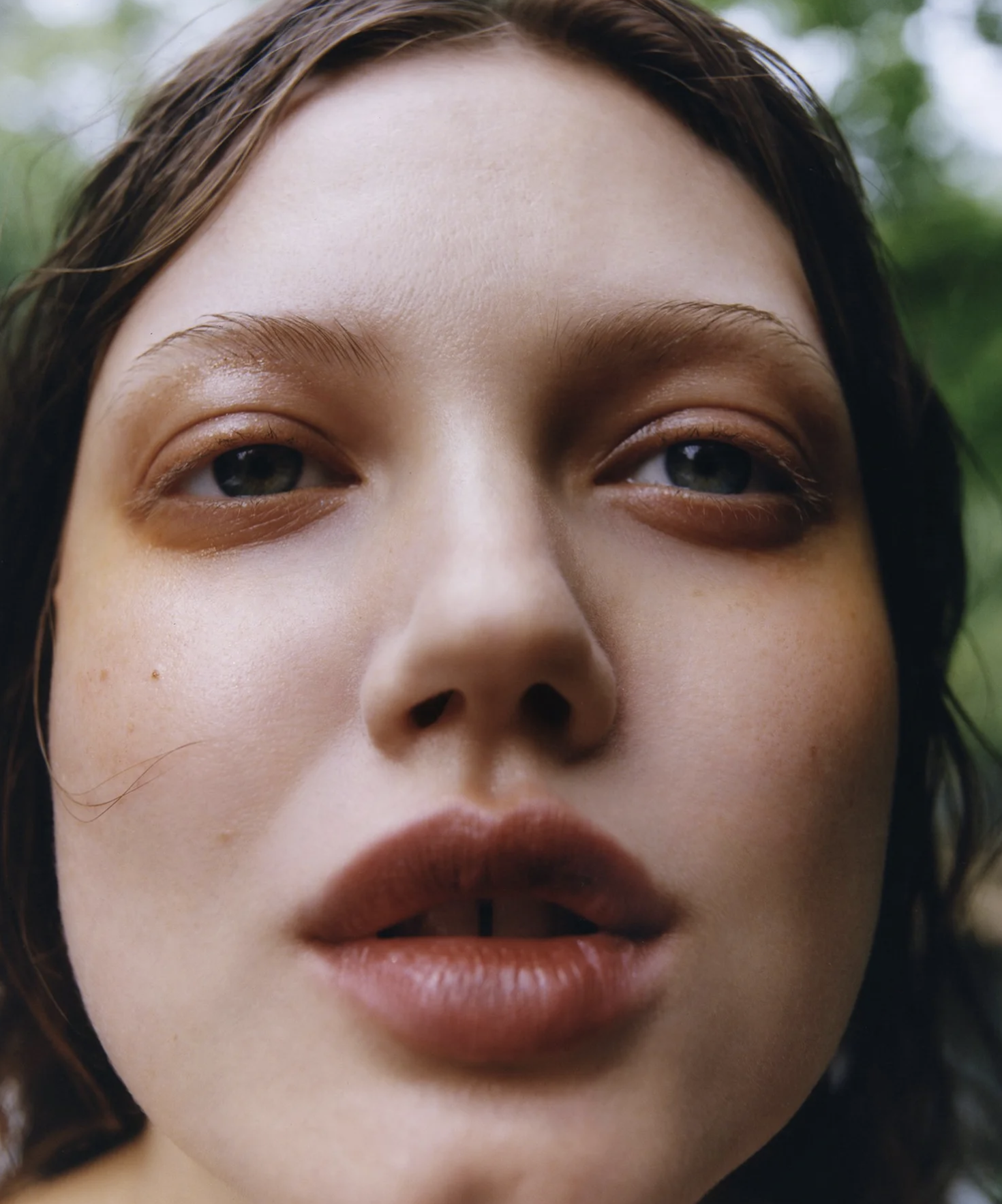 Close-up of a woman's face, focusing on her eyes, nose, and lips, with blurred green background.