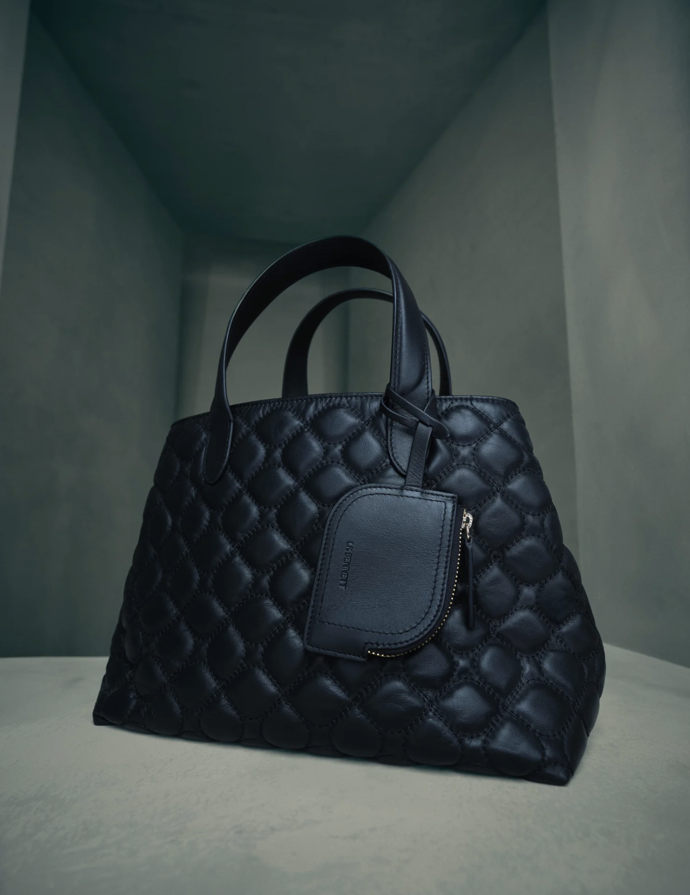 A black quilted handbag with a matching smaller pouch attached via a leather strap, placed on a flat surface against a simple background.