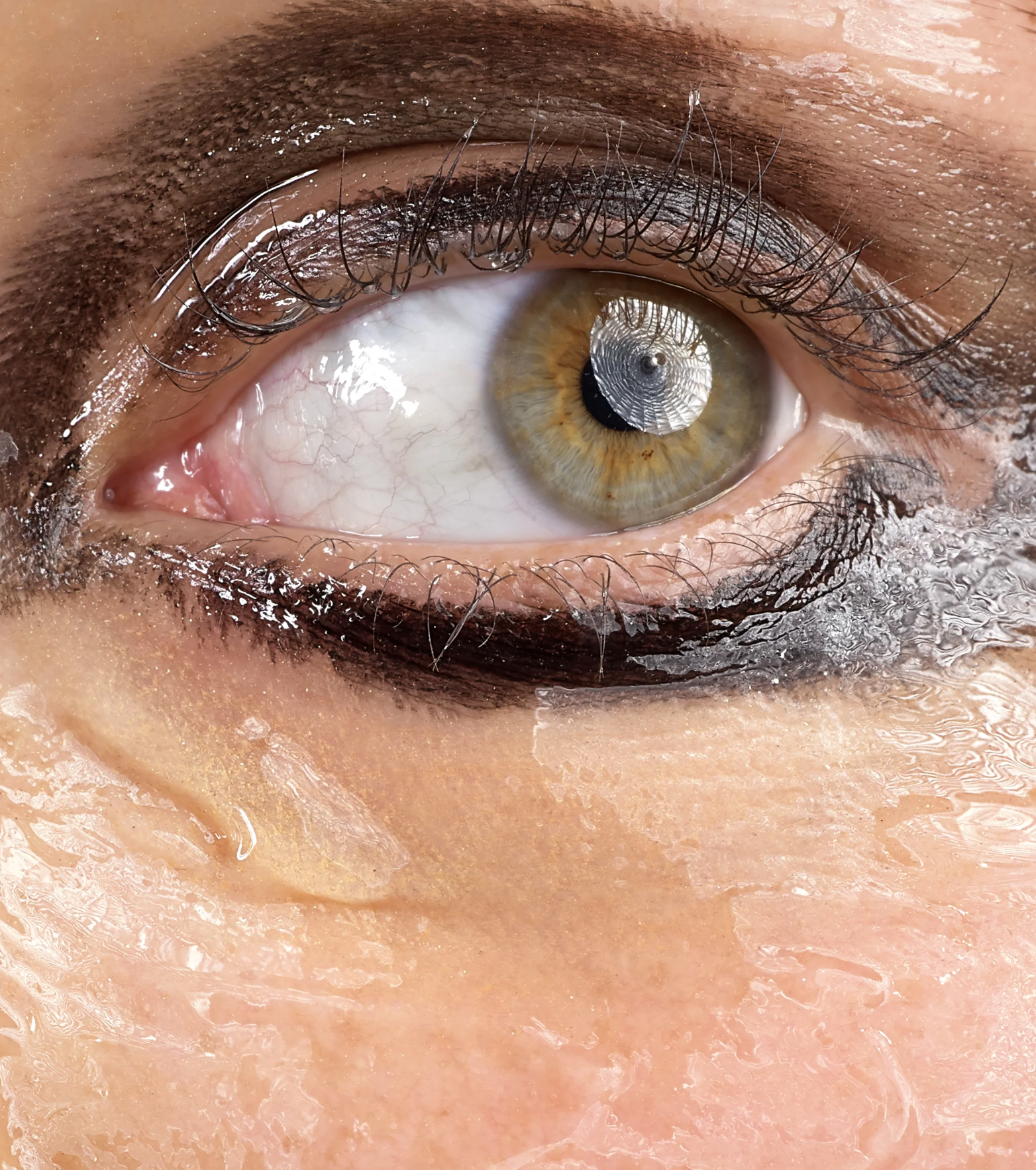 Close-up of a human eye with a hazel iris, surrounded by wet eyelashes and skin, with a reflection of a window or grid pattern in the eye's cornea.