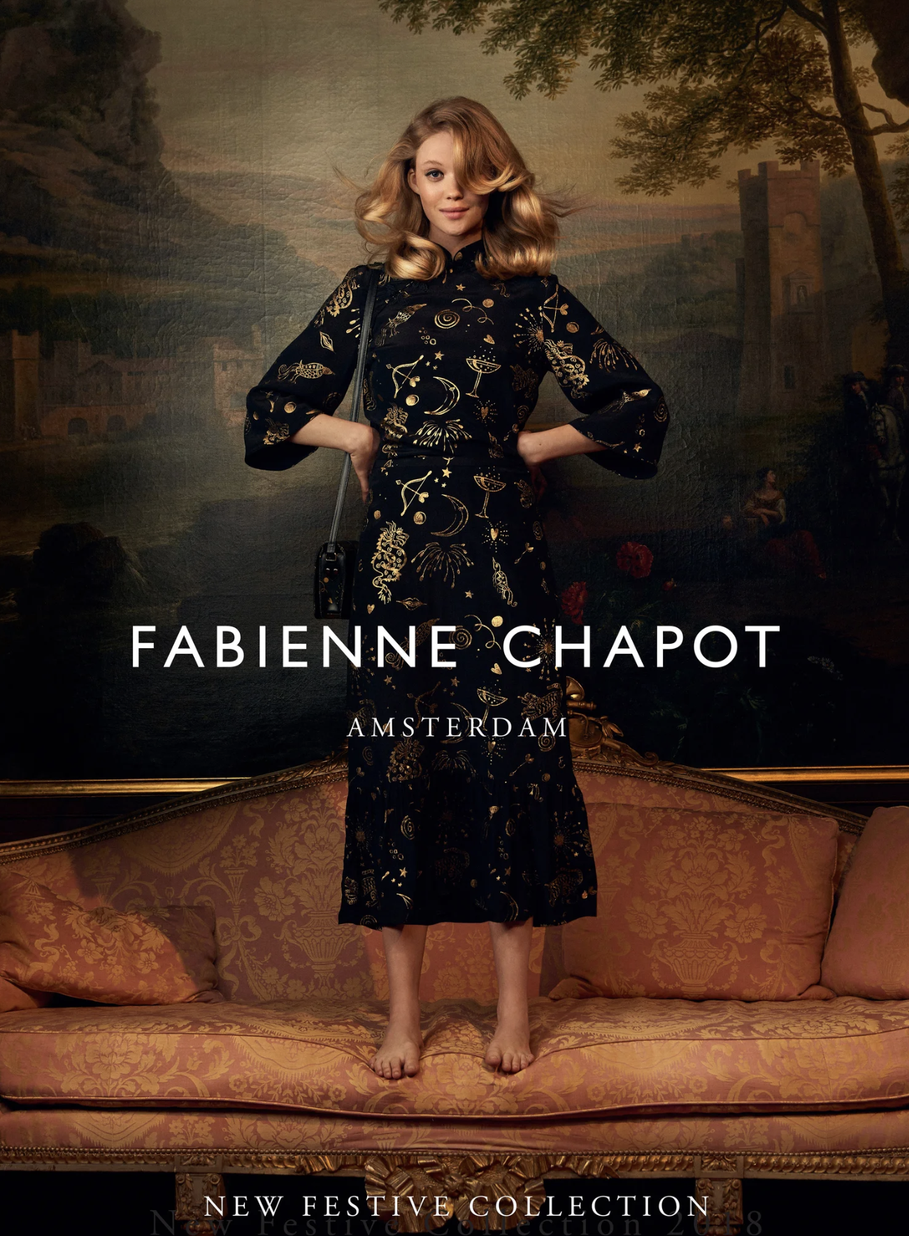 An advertisement featuring a woman with red hair wearing a black dress with gold celestial and zodiac patterns, standing on a vintage-style sofa with a historic landscape painting in the background, promoting the Fabienne Chapot Amsterdam's new festi