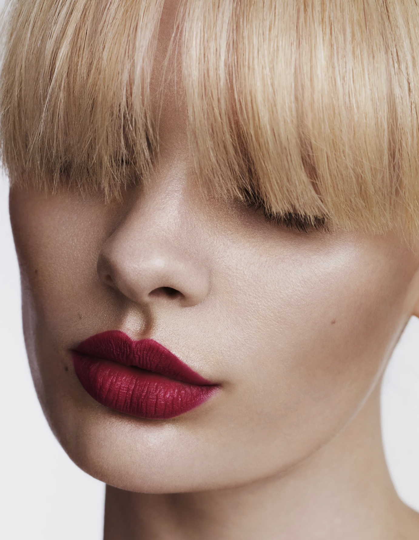 Close-up of a woman with short, blonde hair, red lipstick, and smooth skin.