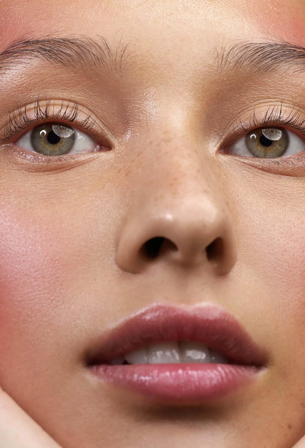 Close-up of a woman's face showing her eyes, nose, and lips with smooth skin, natural makeup, and well-groomed eyebrows.