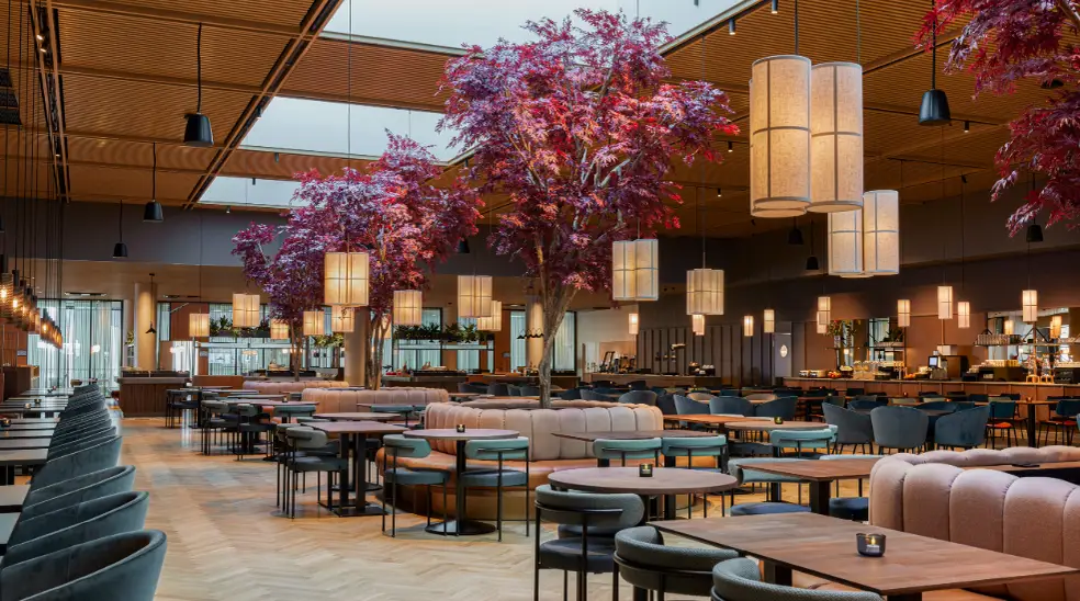 Interior of a modern restaurant or lounge with large pink trees, hanging lamps, and numerous tables and chairs.