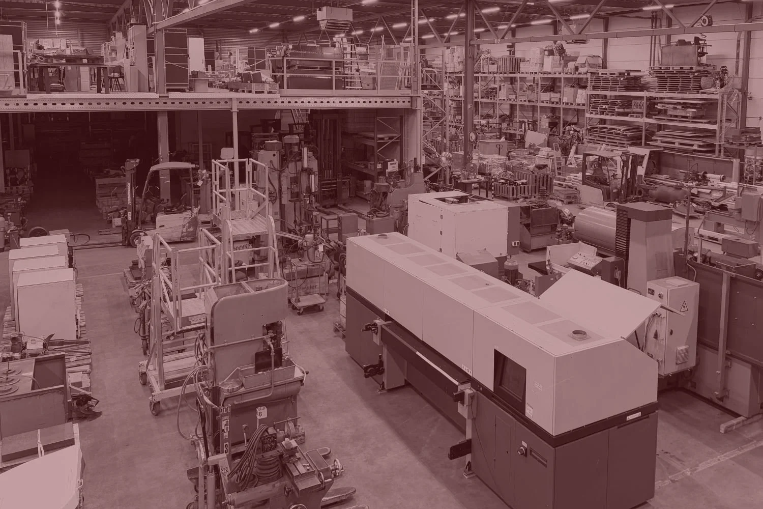 Een grote industriële fabriekshal met verschillende machines, werkstations en opslagrekken gevuld met materialen en onderdelen.