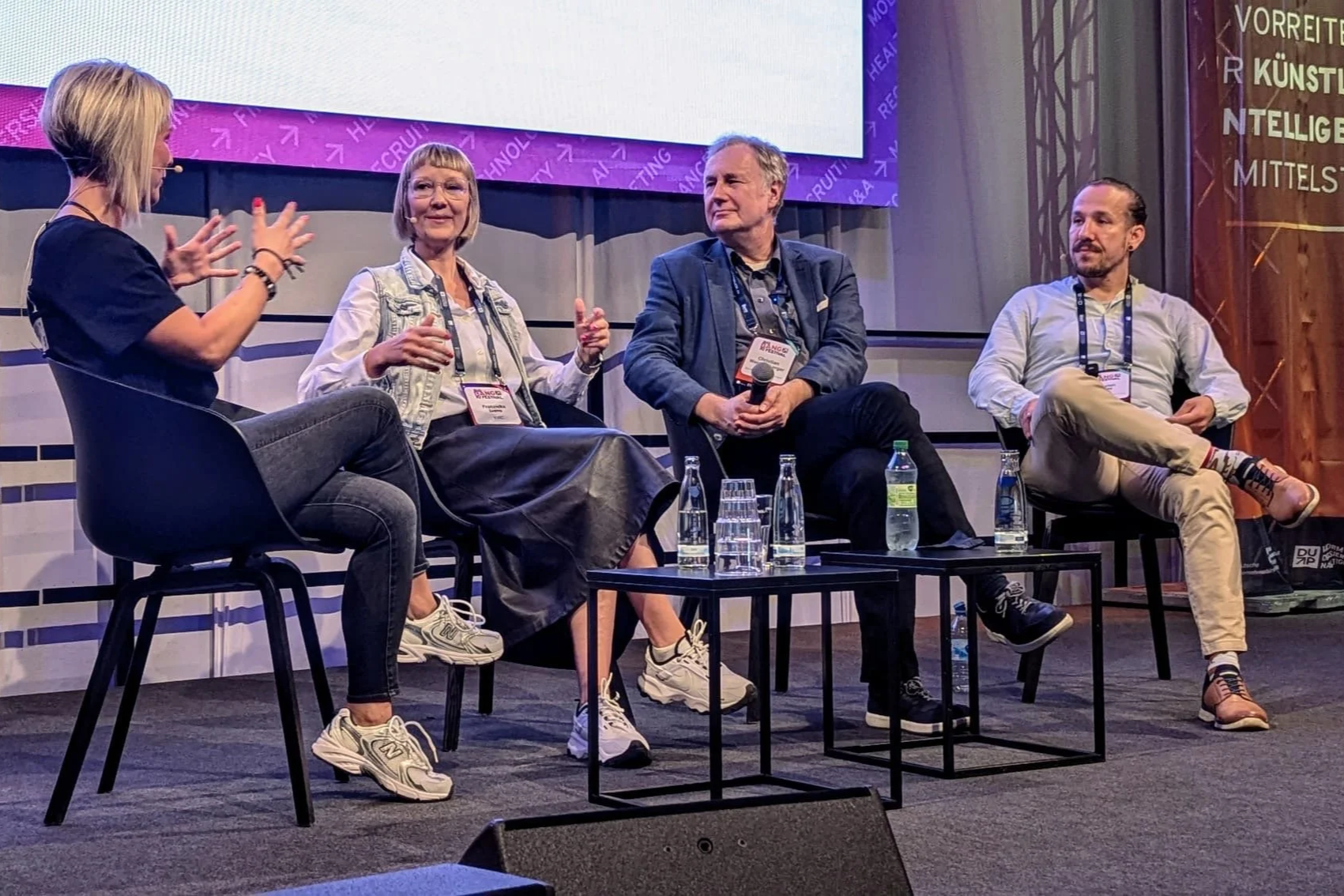 Gesprächsrunde auf einer Bühne mit mehreren Teilnehmenden im Austausch zu Arbeiten mit Krebs
