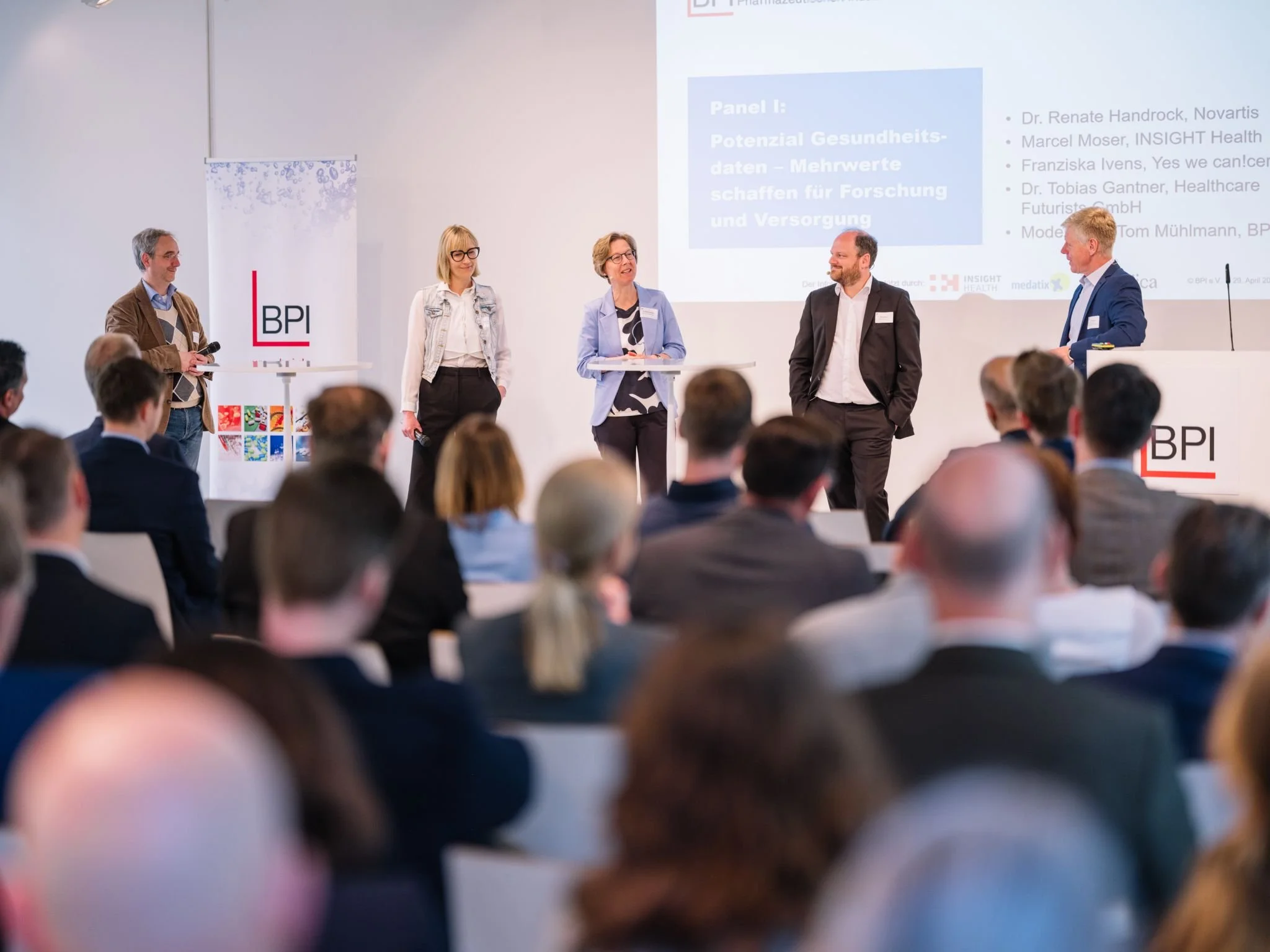 Paneldiskussion auf einer Konferenz mit mehreren Speaker:innen auf der Bühne und Publikum im Saal zu KI und Gesundheit.
