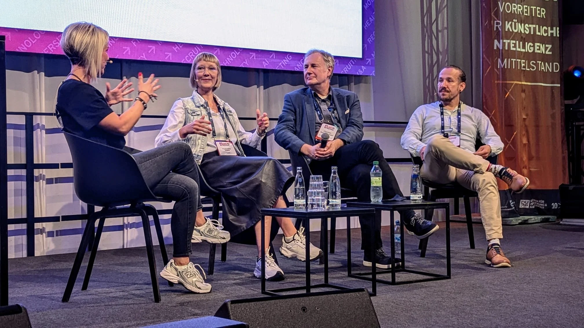 Gesprächsrunde auf einer Bühne mit mehreren Teilnehmenden im Austausch zu Arbeiten mit Krebs